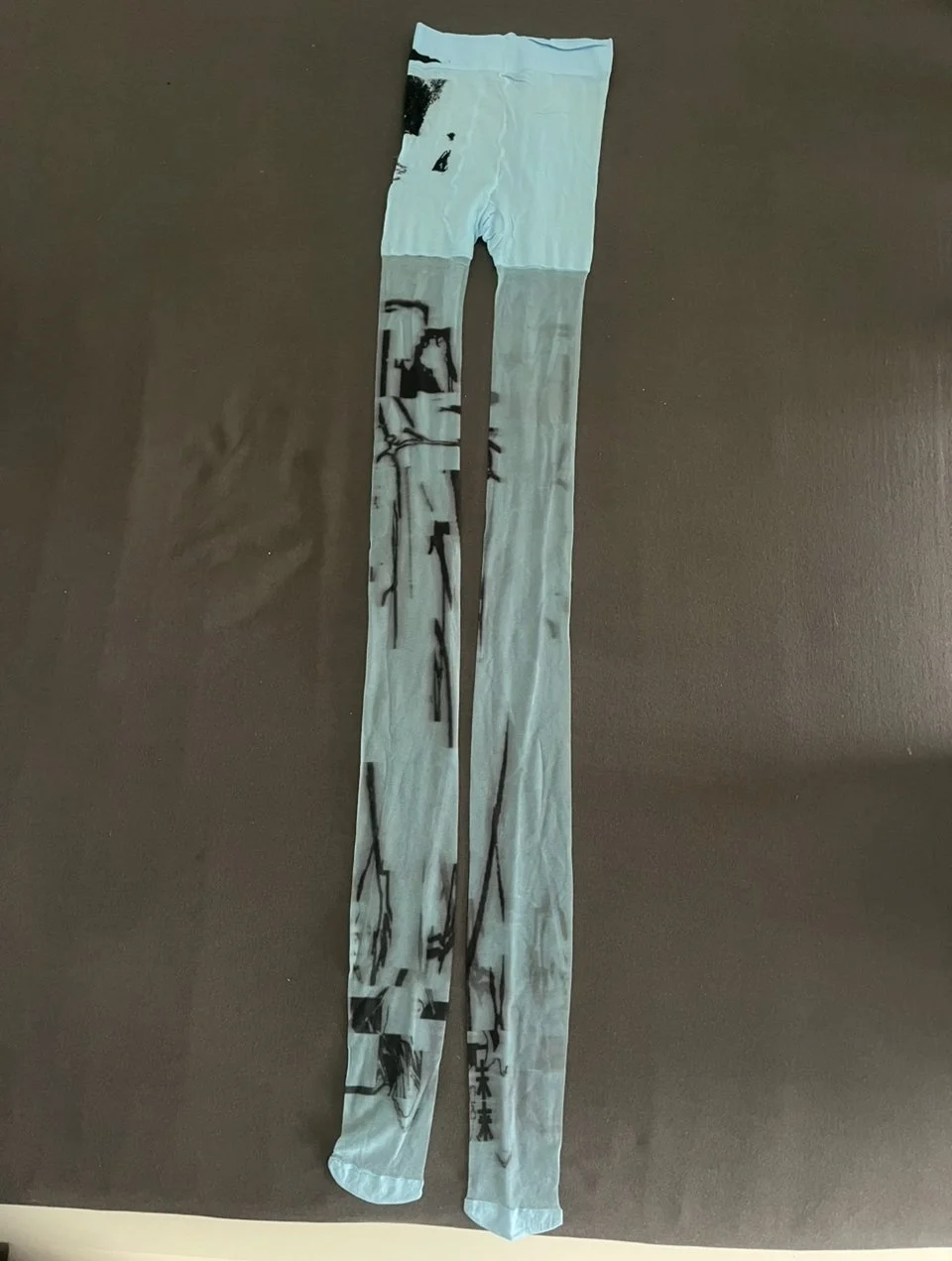 Front view of sheer blue tights with black tattoo-style line art and Chinese text printed down the legs.