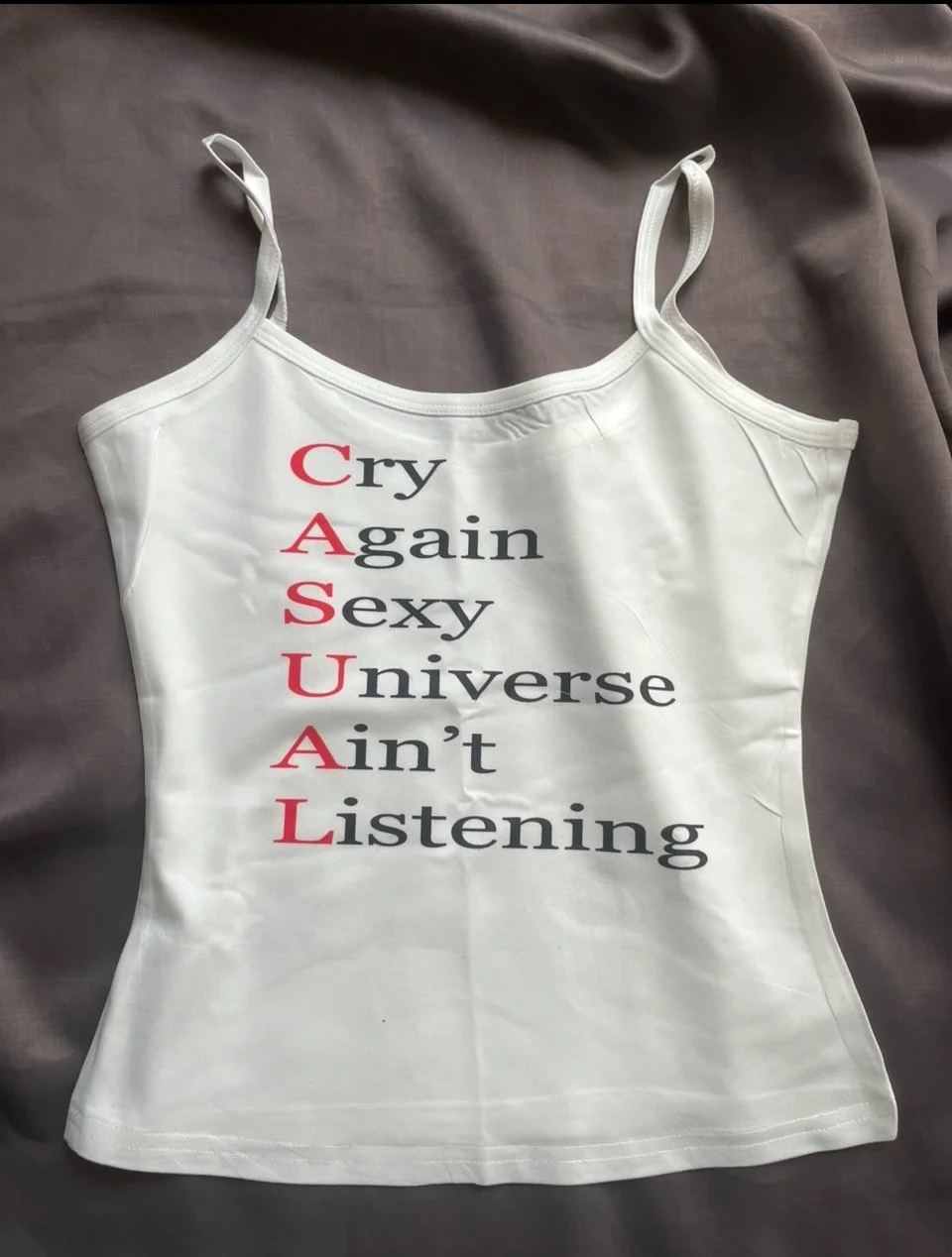 White camisole featuring bold "Cry Again Sexy Universe Ain’t Listening" print. A sarcastic, slim-fit piece for emotionally detached dressers.