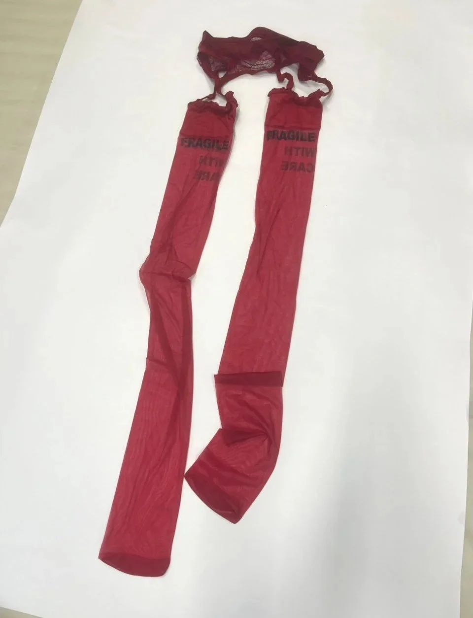 Angled view of provocative red lingerie stockings featuring printed warning text and intricate lace waistband.