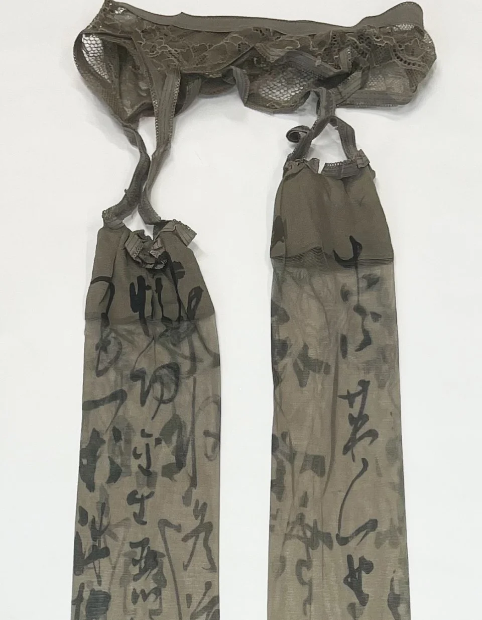 Grey calligraphy-print sheer stockings laid flat with script visible along both legs and lace waistband