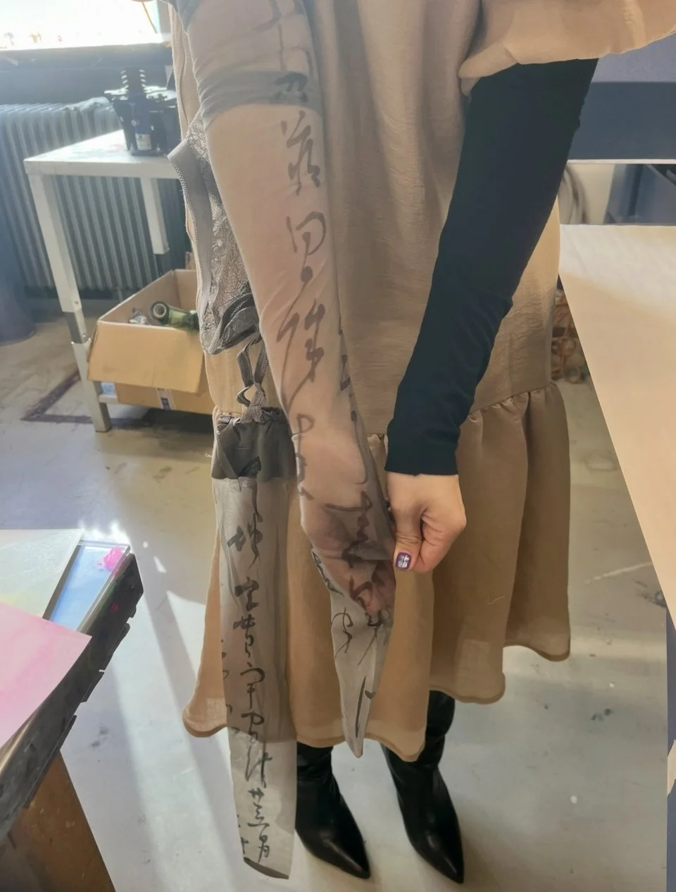 Model holding grey sheer calligraphy-print stocking, showing script details against brown dress