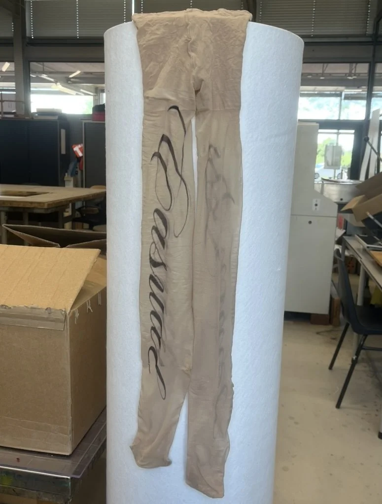 Artisanal Y2K-inspired tights in translucent mesh, featuring oversized black cursive text. Subversive legwear for contemporary girlhood aesthetics.