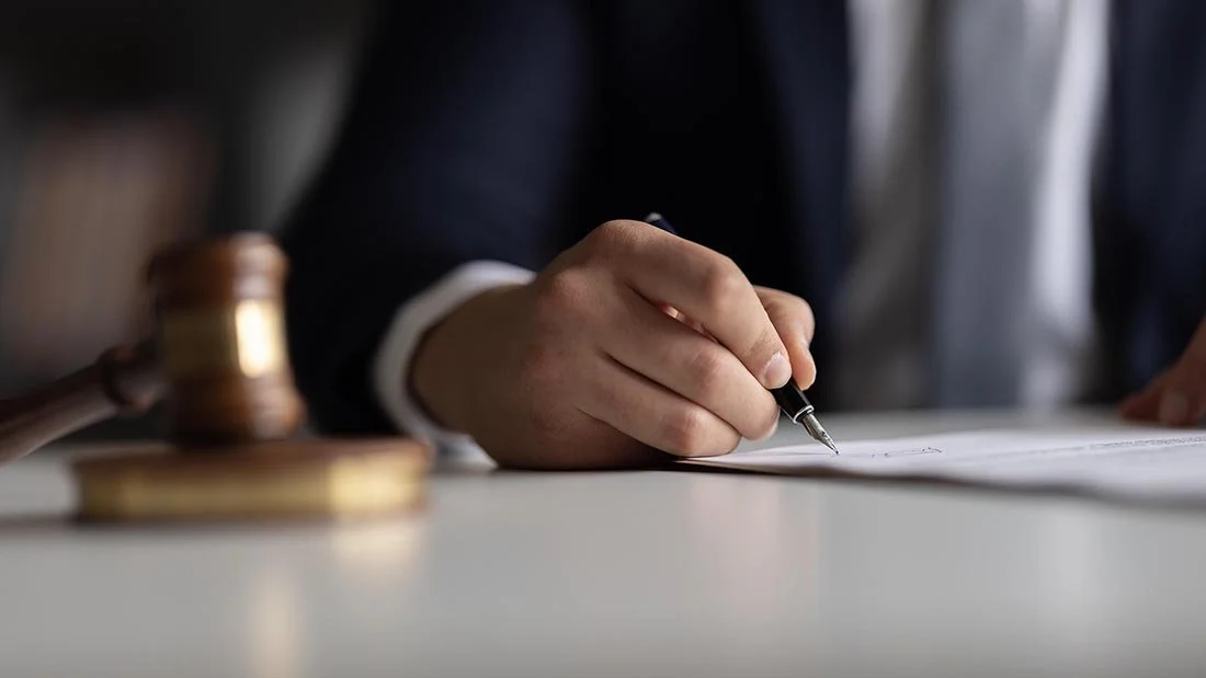 close up of hand of man in suit signing legal document with fountain pen