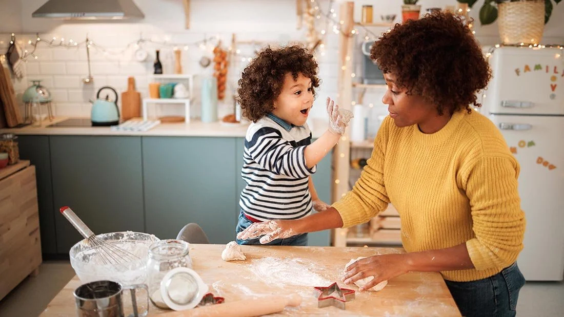 black mother baking with playful daughter in warm and colorful kitchen