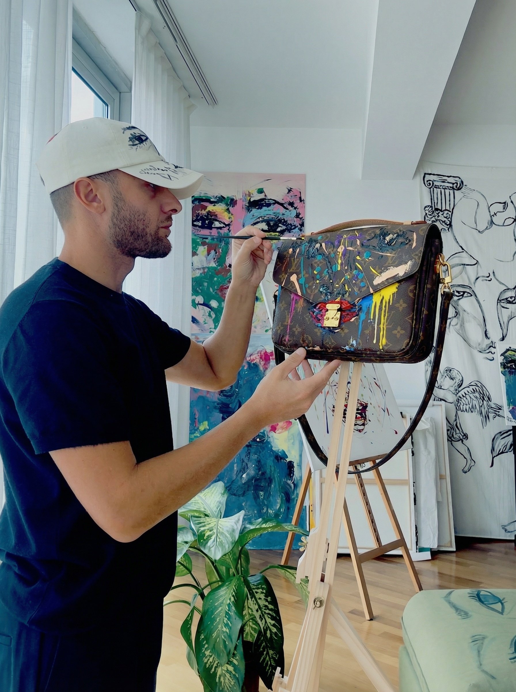 Un uomo mentre dipinge una borsa Louis Vuitton con vernice colorata in un atelier d'arte.