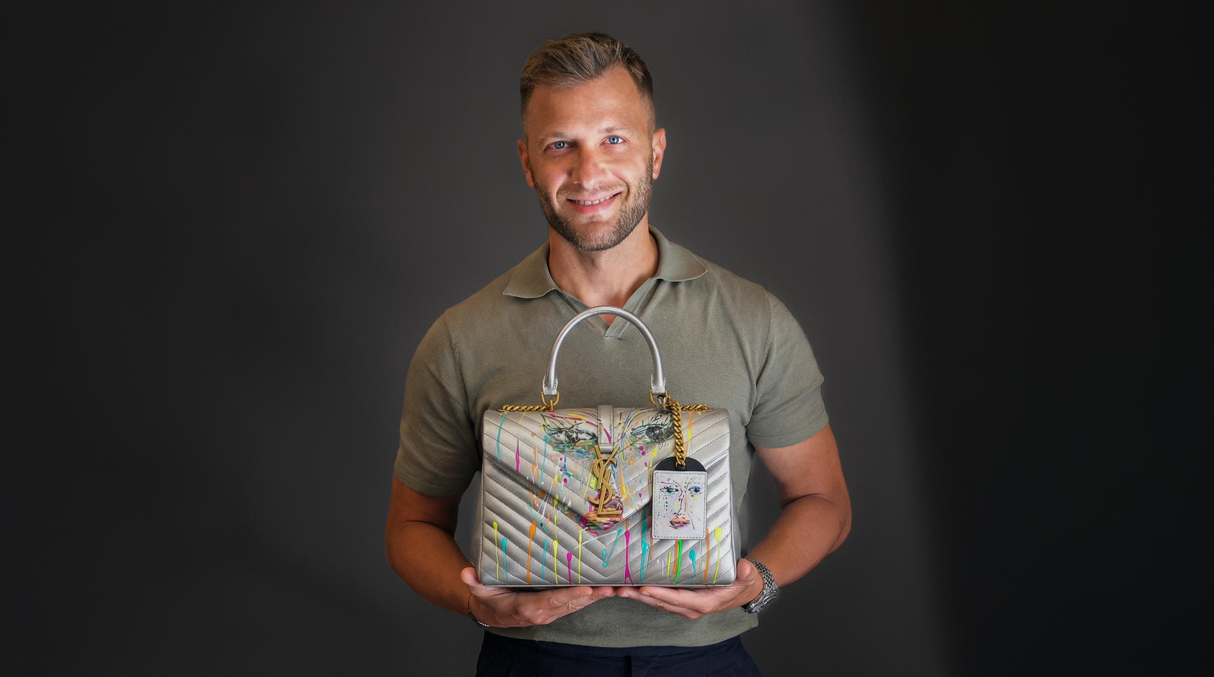 Uomo sorridente che mostra una borsa da sera colorata con disegni di spray, con la scritta Yves Saint Laurent