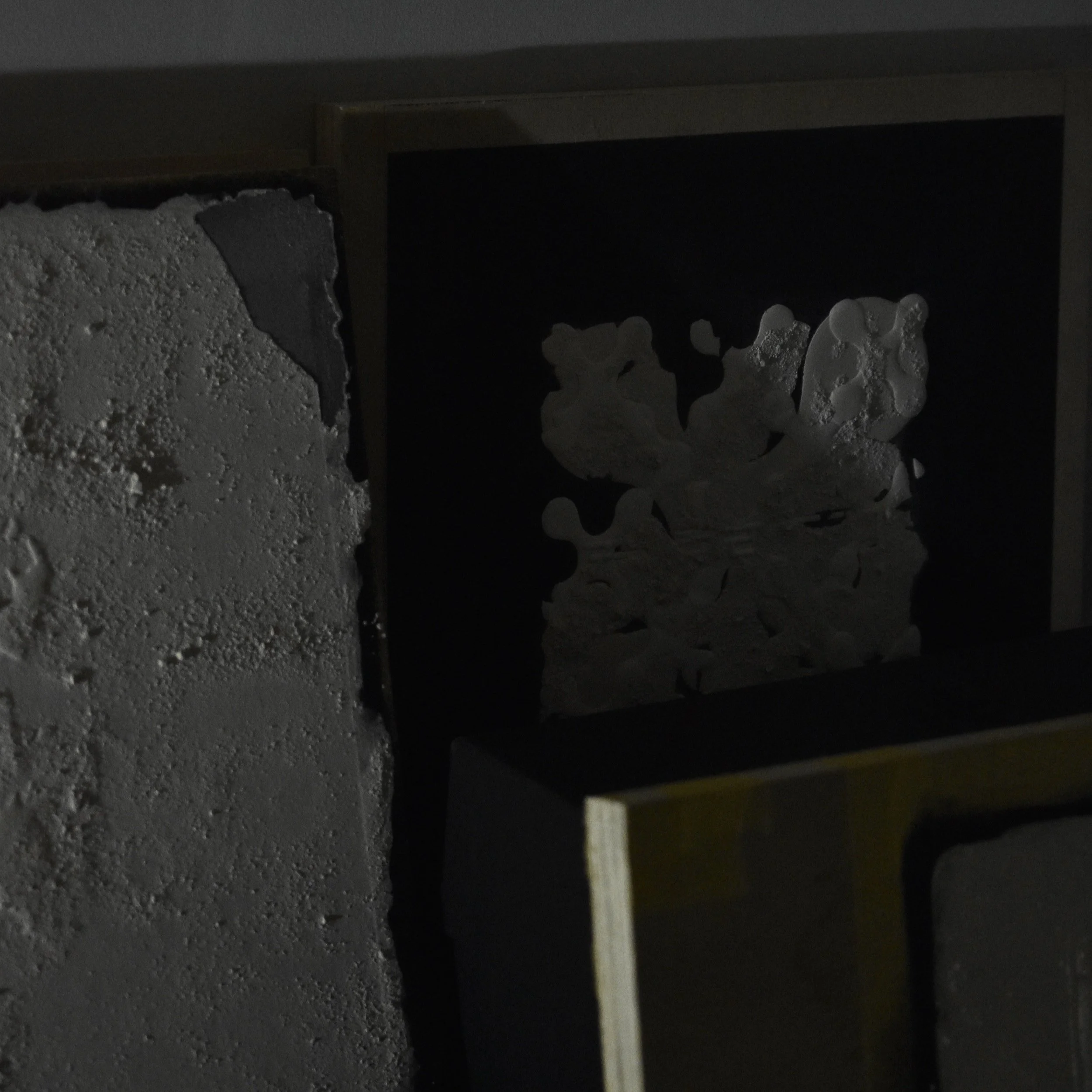 Abstract textured art pieces with dark and light contrasts leaning against a wall.
