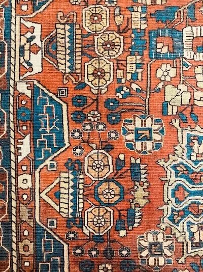Close-up of a traditional patterned rug featuring geometric floral motifs in red, blue, cream, and yellow colors.