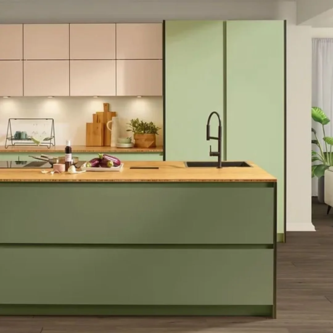 Modern kitchen with light green cabinets, wooden countertop, black faucet, potted plant, and decorative cutting boards.