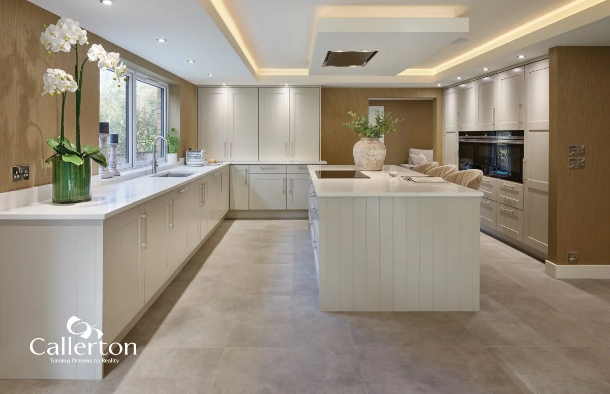 Modern kitchen with white cabinets, a large central island with a vase and plant, a side window with greenery outside, and neutral decor.