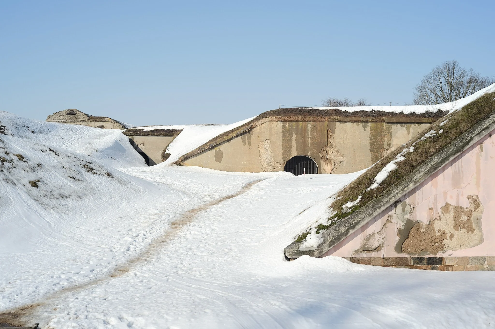 Snow-covered fort with walls and a tunnel entrance, under a clear blue sky.