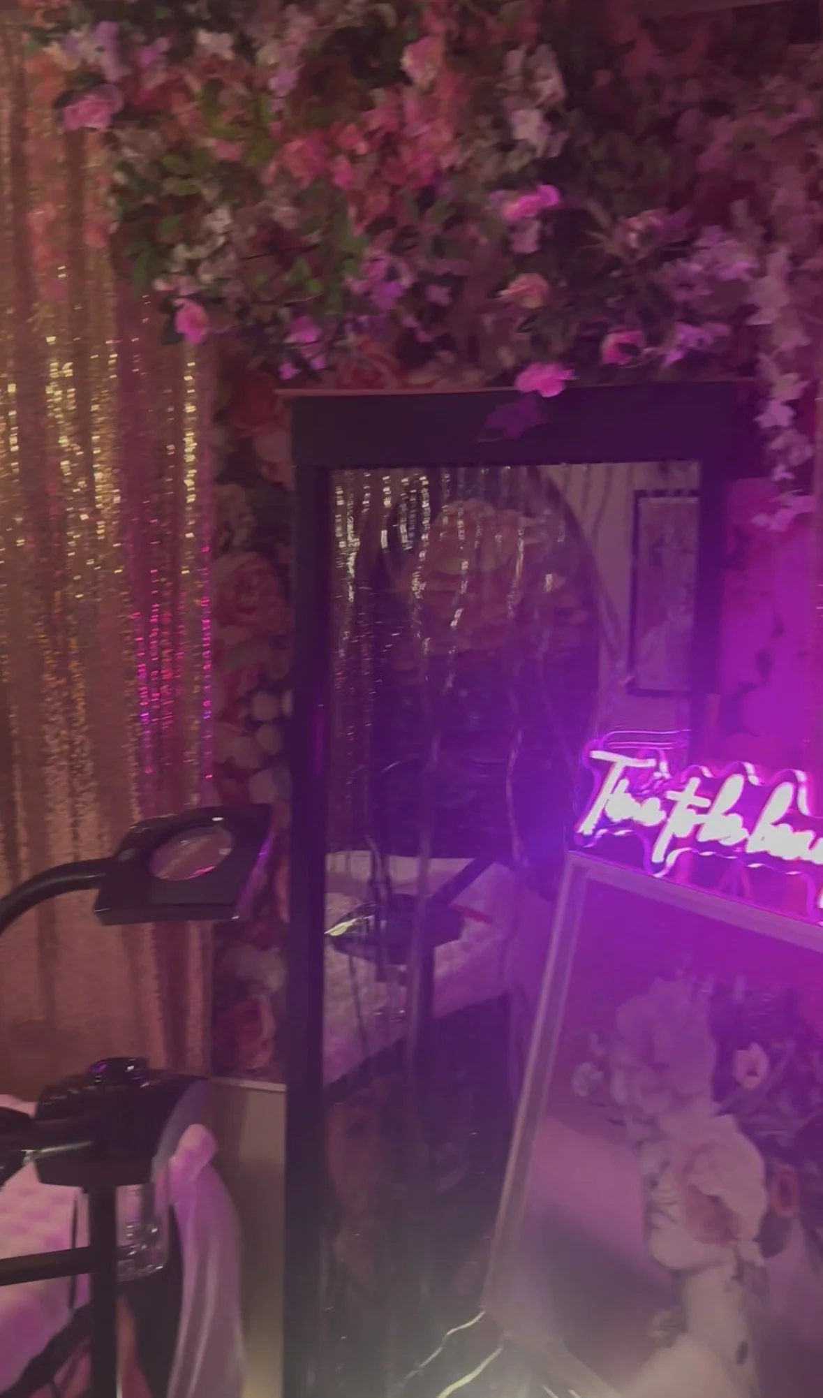 Interior of a room with pink flowers, a neon pink sign, a mirror, and decorative artwork.