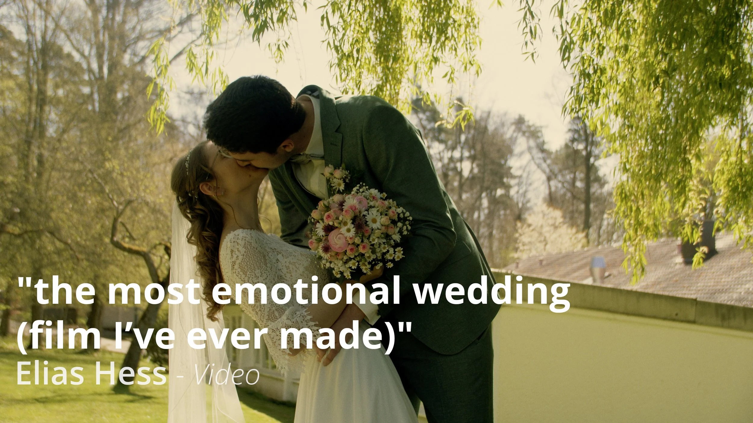 Ein Brautpaar umarmt sich und küsst sich bei Sonnenuntergang im Freien, mit Bäumen im Hintergrund und einem Dach. Die Braut trägt ein weißes Hochzeitskleid mit Spitzenärmeln, der Bräutigam einen grauen Anzug, und sie hält einen Blumenstrauß. Es ist eine romantische Szene, geeignet für Hochzeitswerbung oder -dokumentation.