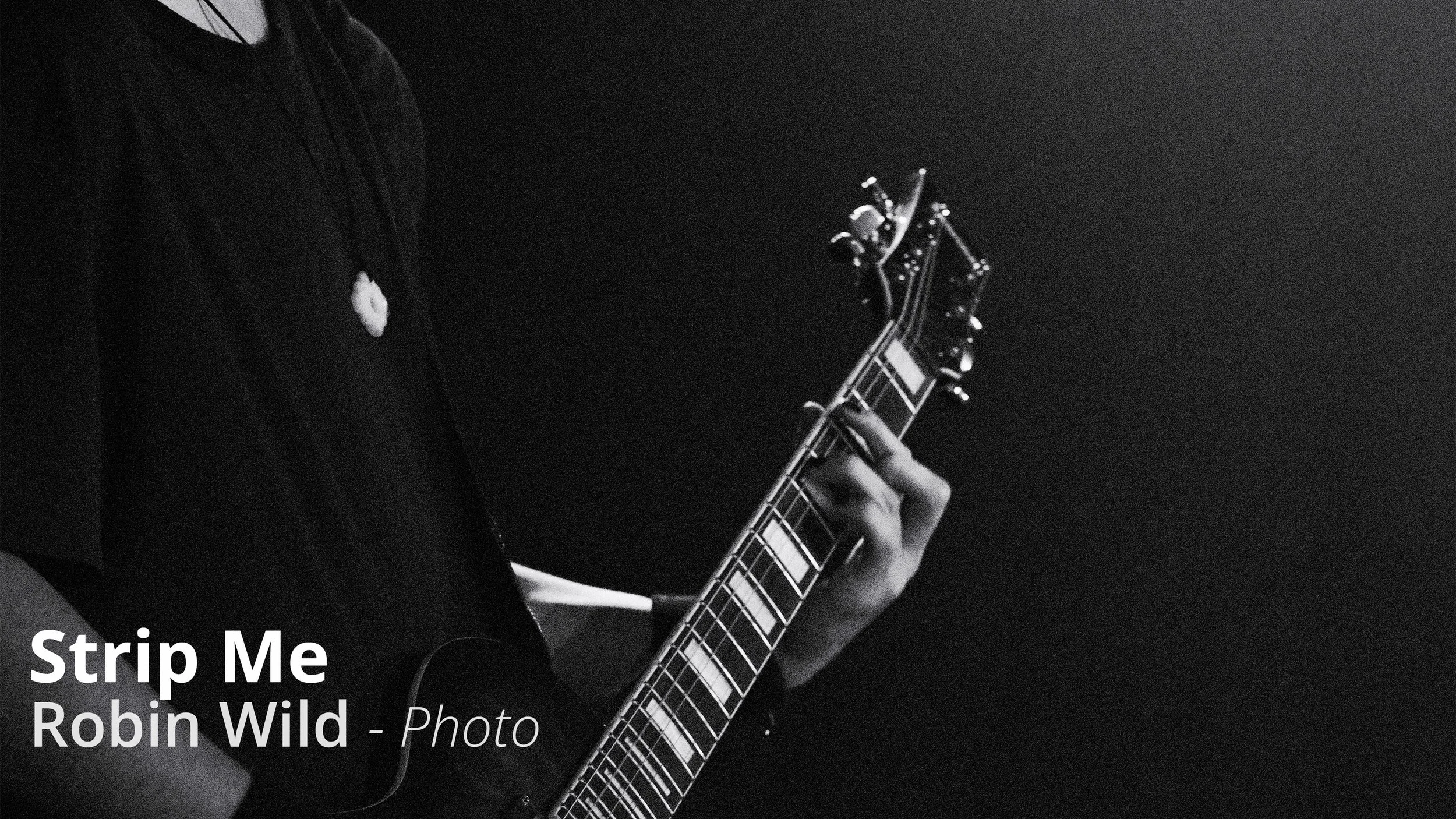 Ein Mensch spielt Gitarre in Schwarz-Weiß, der Fokus liegt auf der Hand, die auf den Saiten liegt, im dunklen Hintergrund.