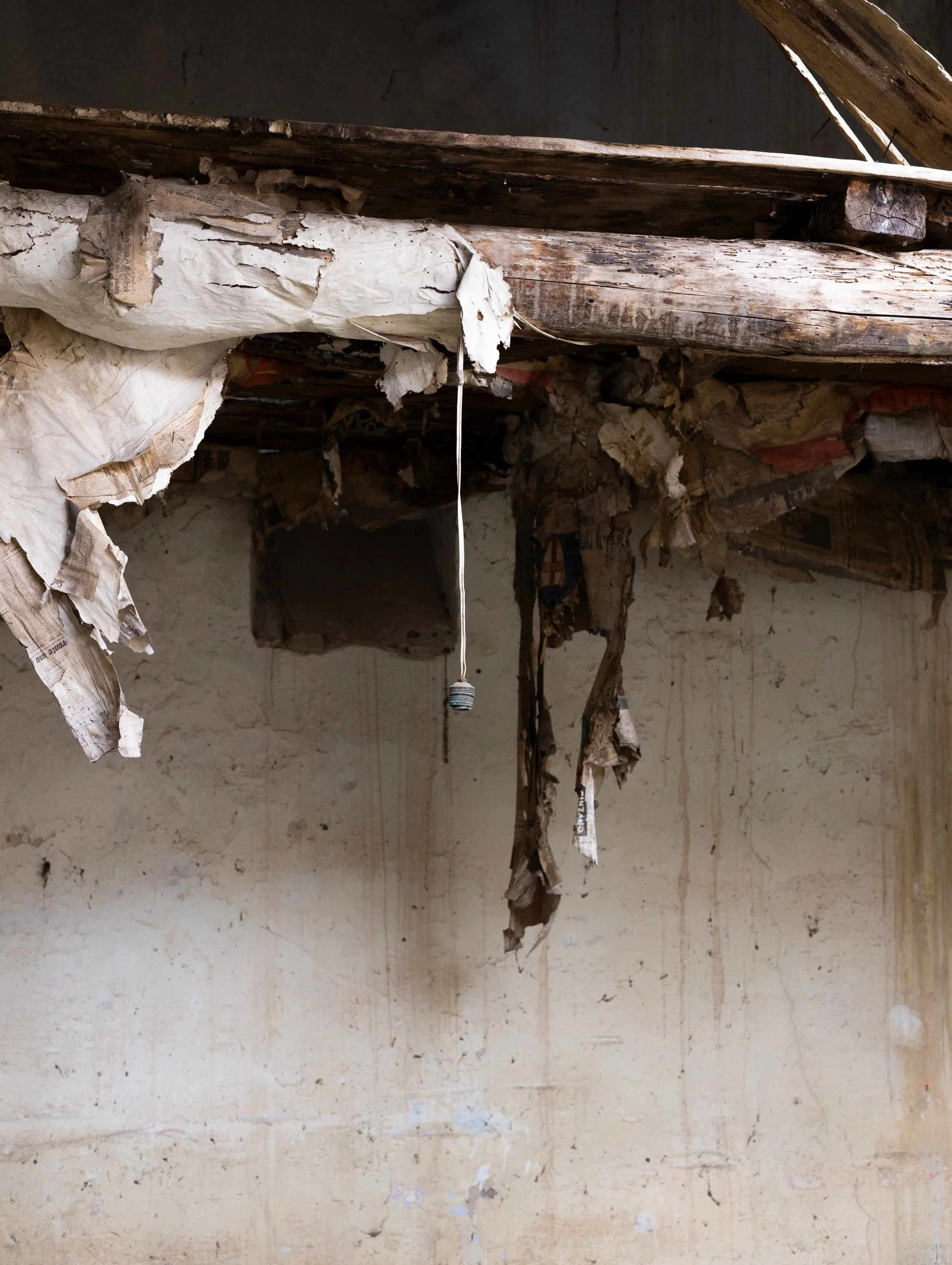 Plafond endommagé avec des morceaux de papier et de bois suspendus, pièce abandonnée avec murs sales et dégradés.