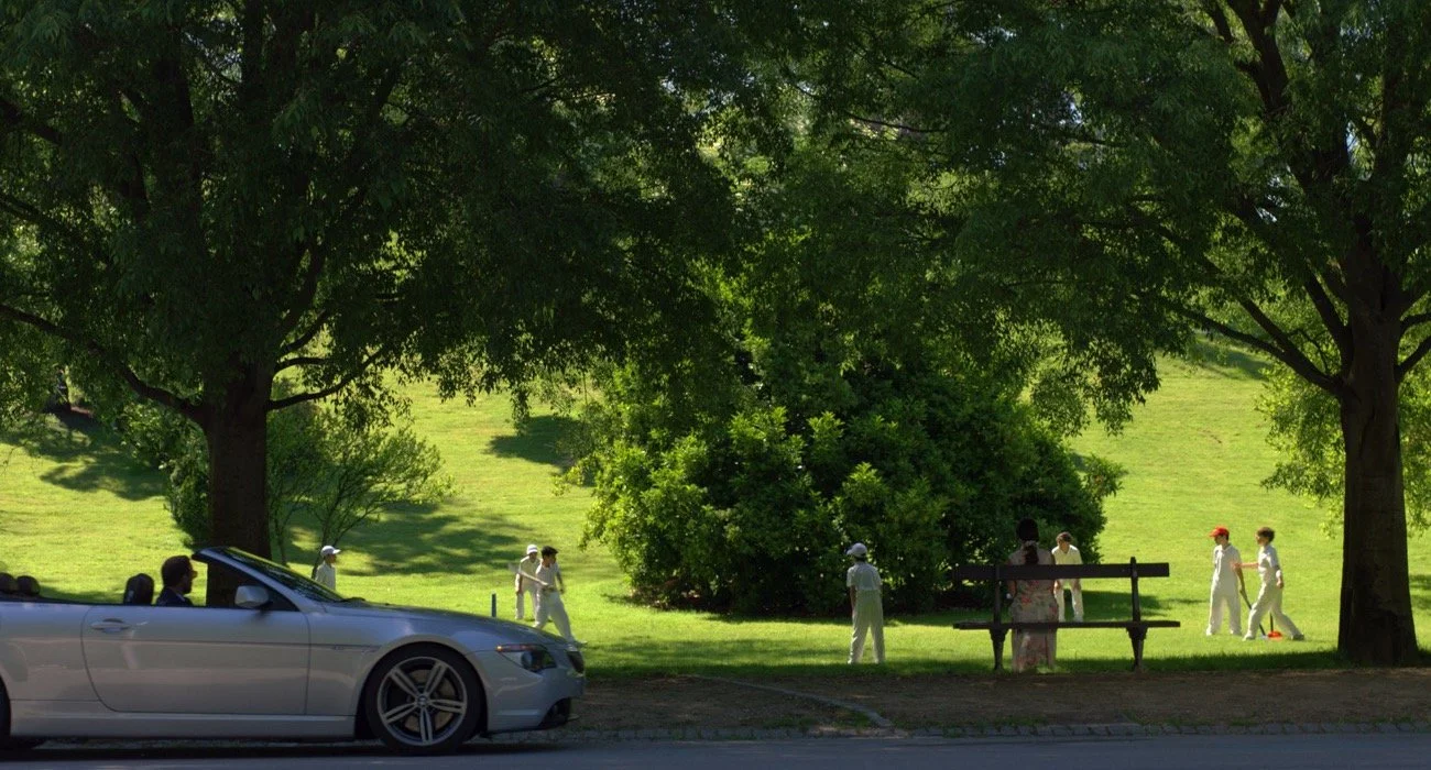 AB de Villiers en un parque con arbustos y árboles verdes, y un coche estacionado en la calle.