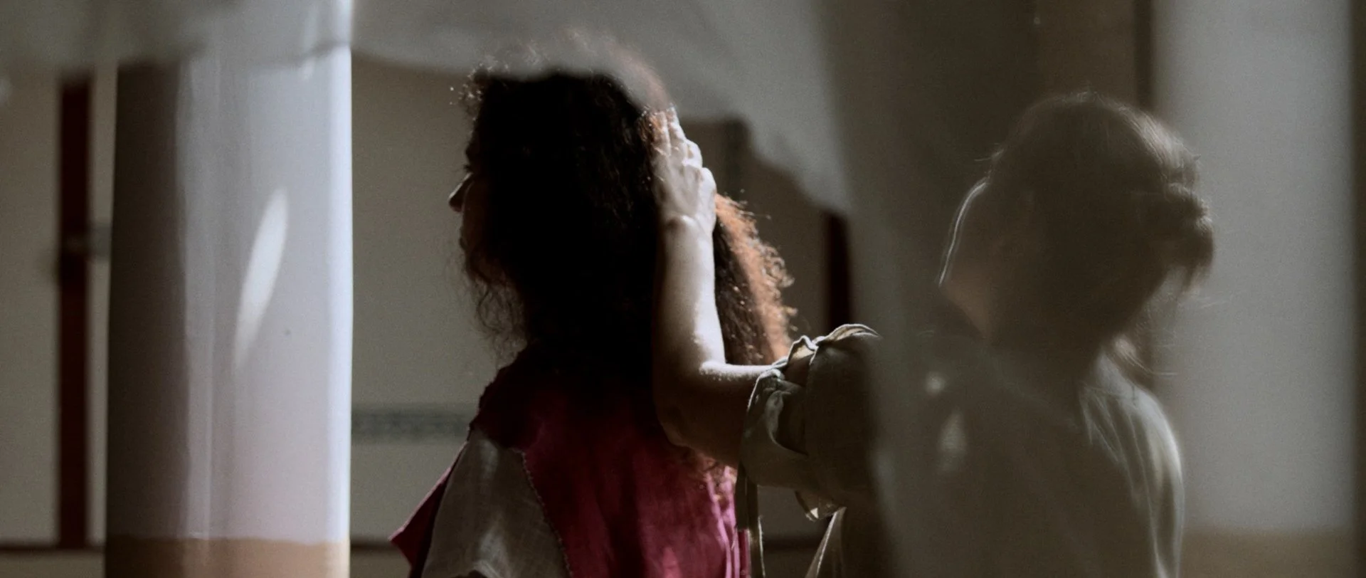 Dos niñas en una habitación, una tocando la cara de la otra, en un ambiente con poca luz.