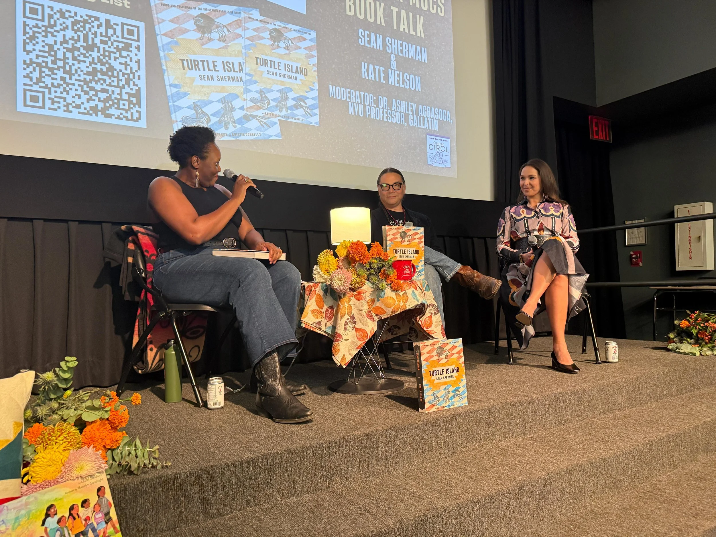 Photo of three people, seated in conversation on a stage