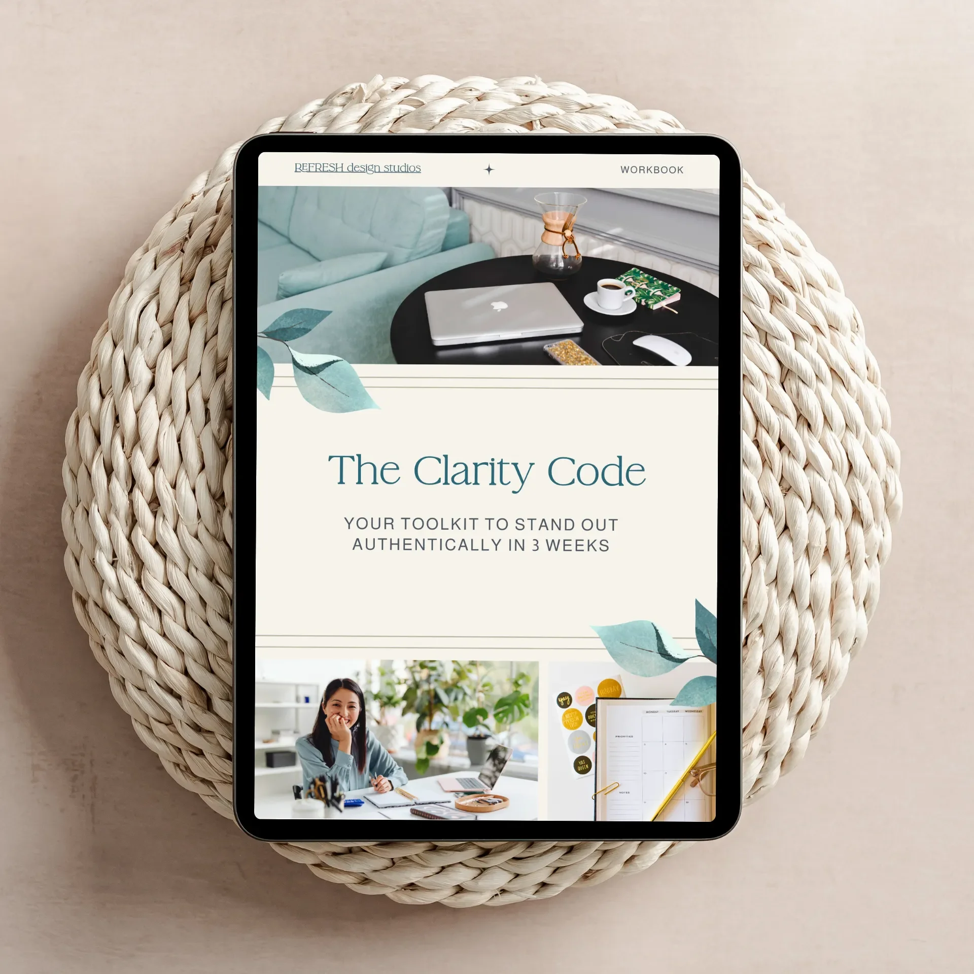 Digital tablet showing a workbook titled 'The Clarity Code' with a subtitle about standing out authentically in 3 weeks, placed on a woven round placemat, with an image of a woman working at her desk and a decorated workspace visible.