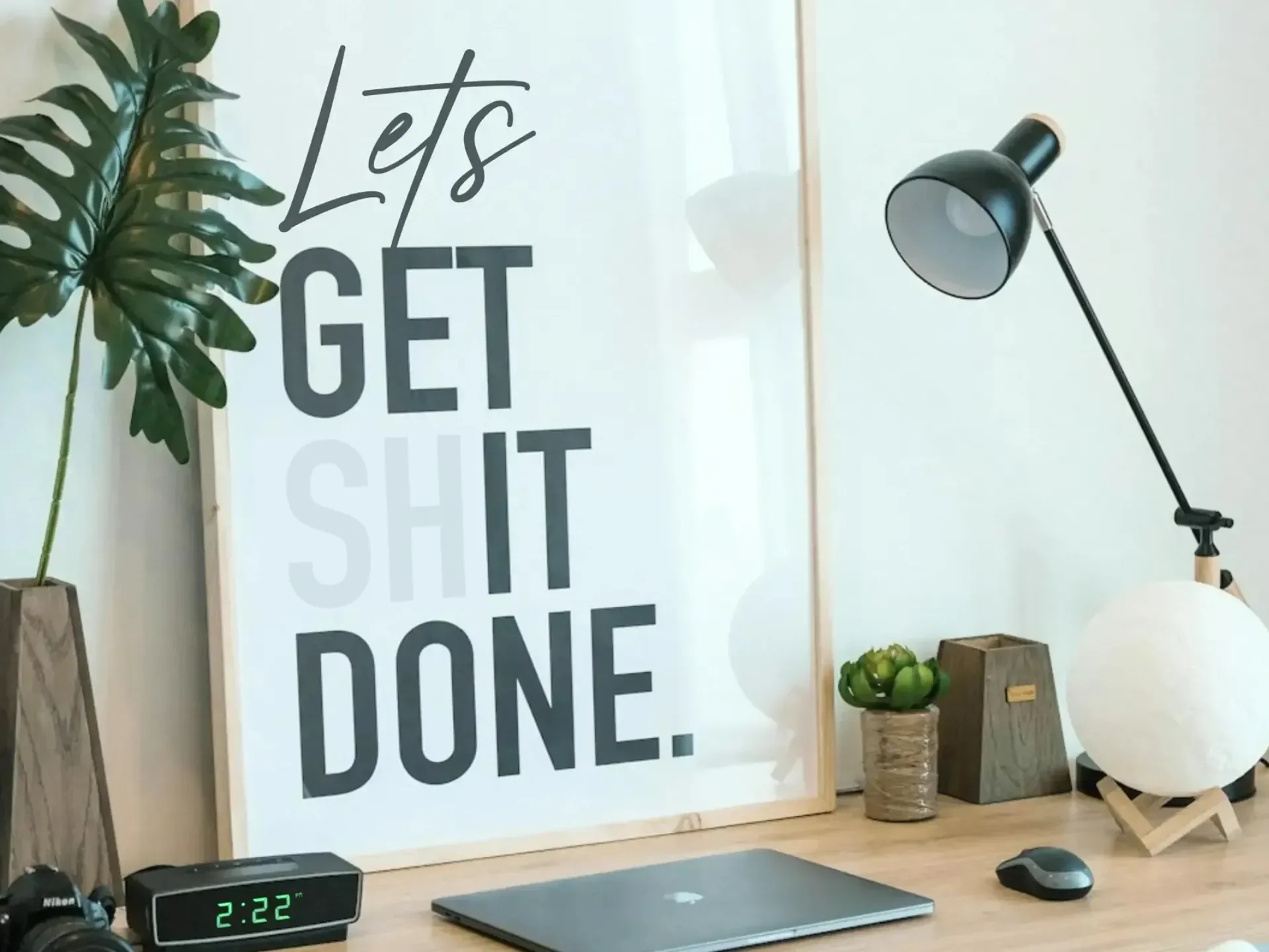 Design with Apple laptop, lamp, clock, plant stem, and sign that says Let's get Shit Done with the Sh faded out.