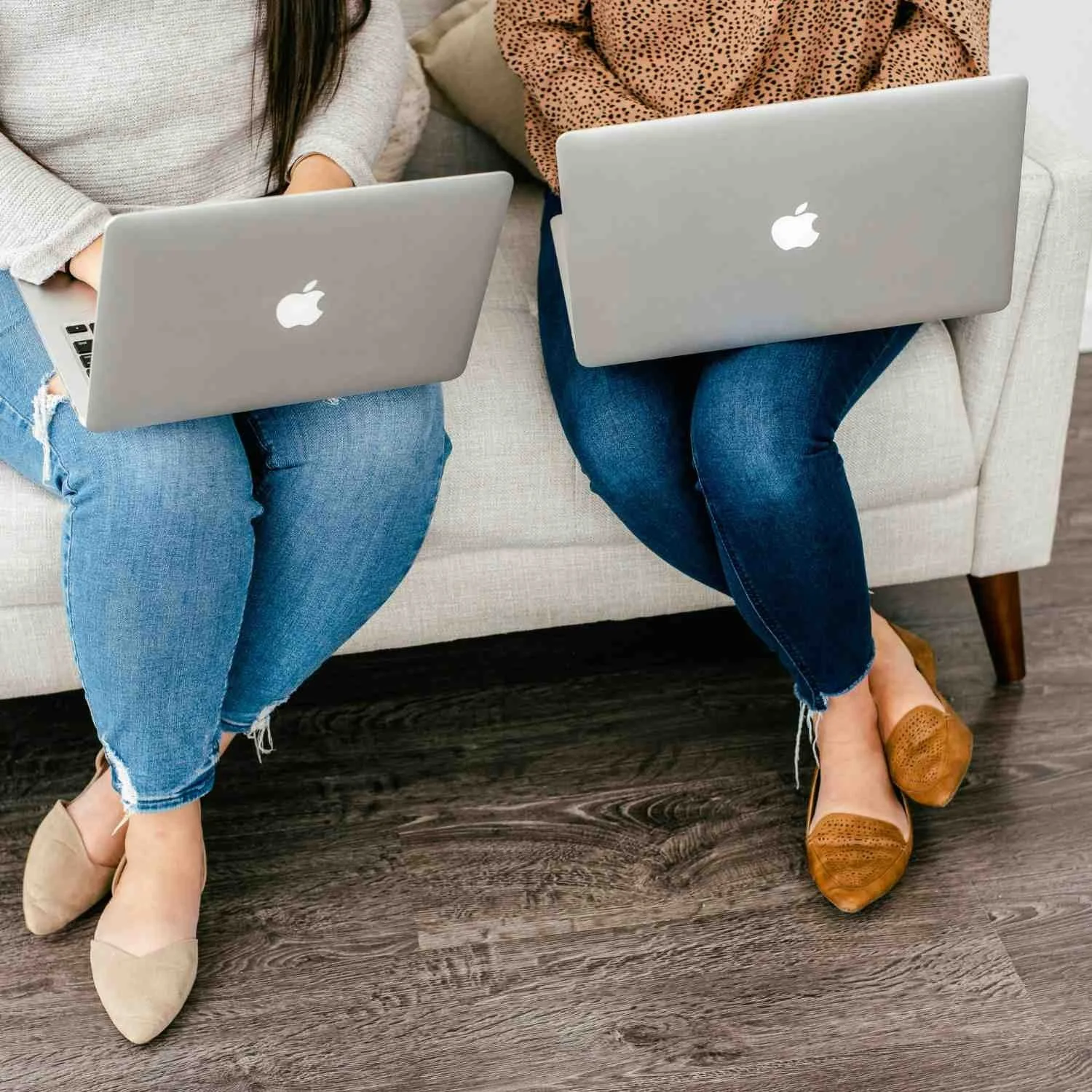 Two women sitting typing on laptops on their laps
