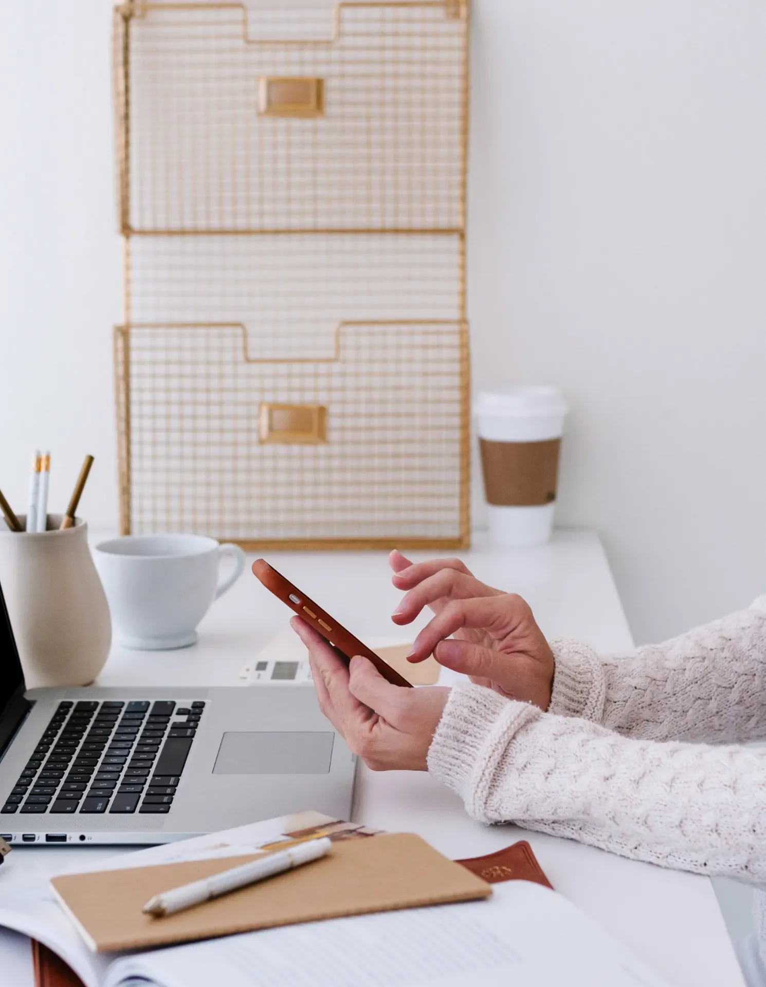woman's hand holding a mobile phone on a desk with a laptop and other office matierals