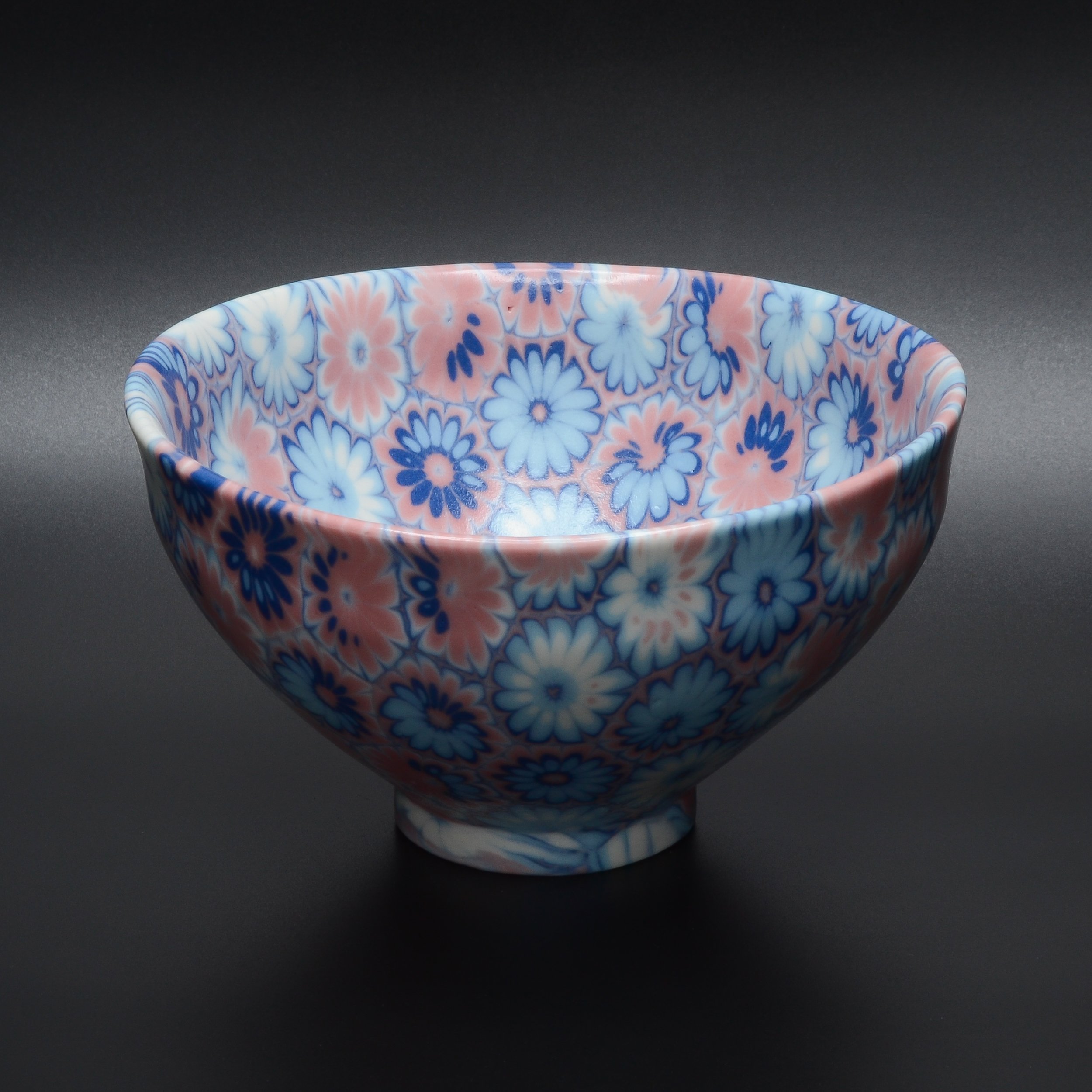 Un bol en porcelaine avec un motif floral coloré en nuances de bleu, blanc et rose posé sur une surface noire.
