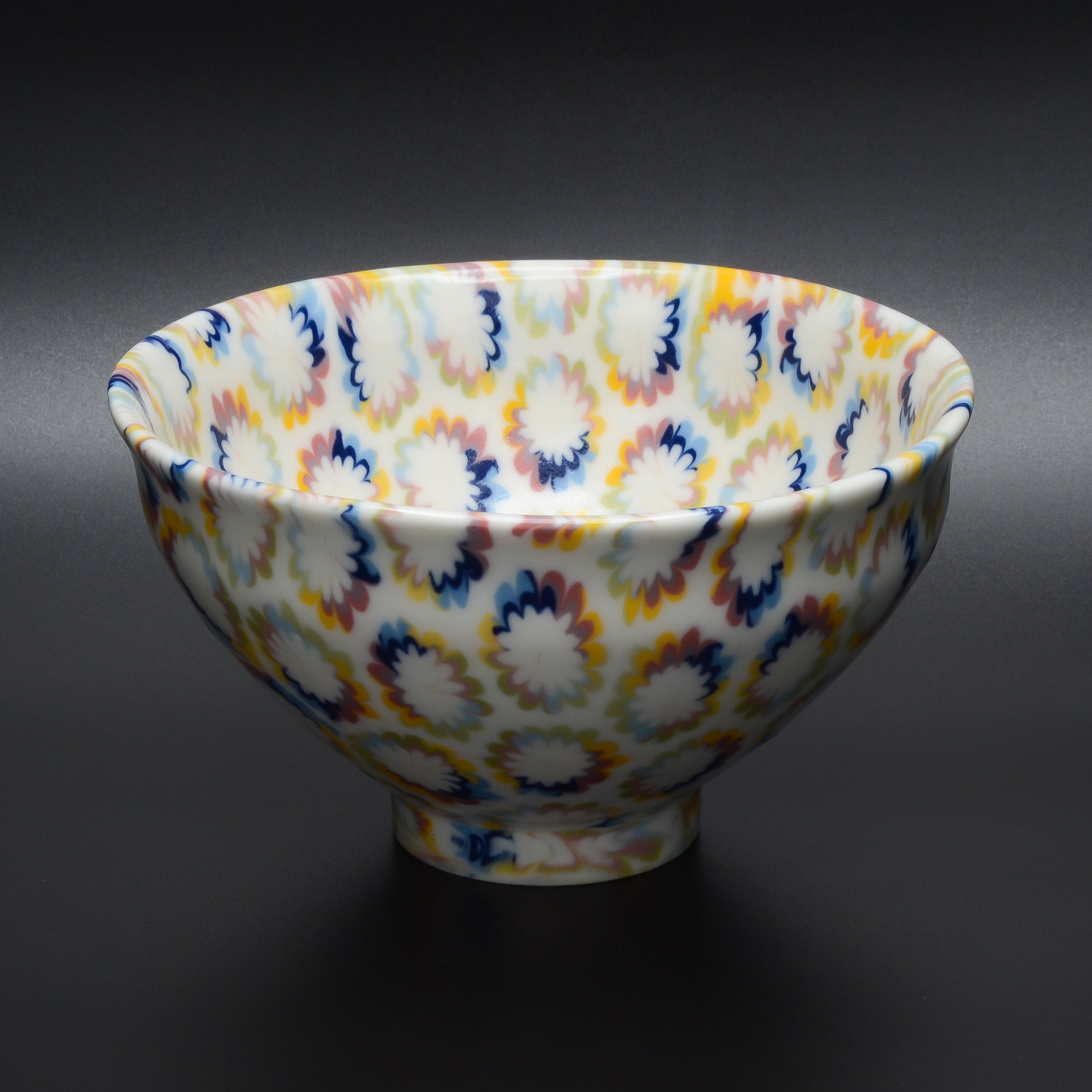 Un bol en porcelaine avec un motif floral coloré, placé sur un fond gris foncé.