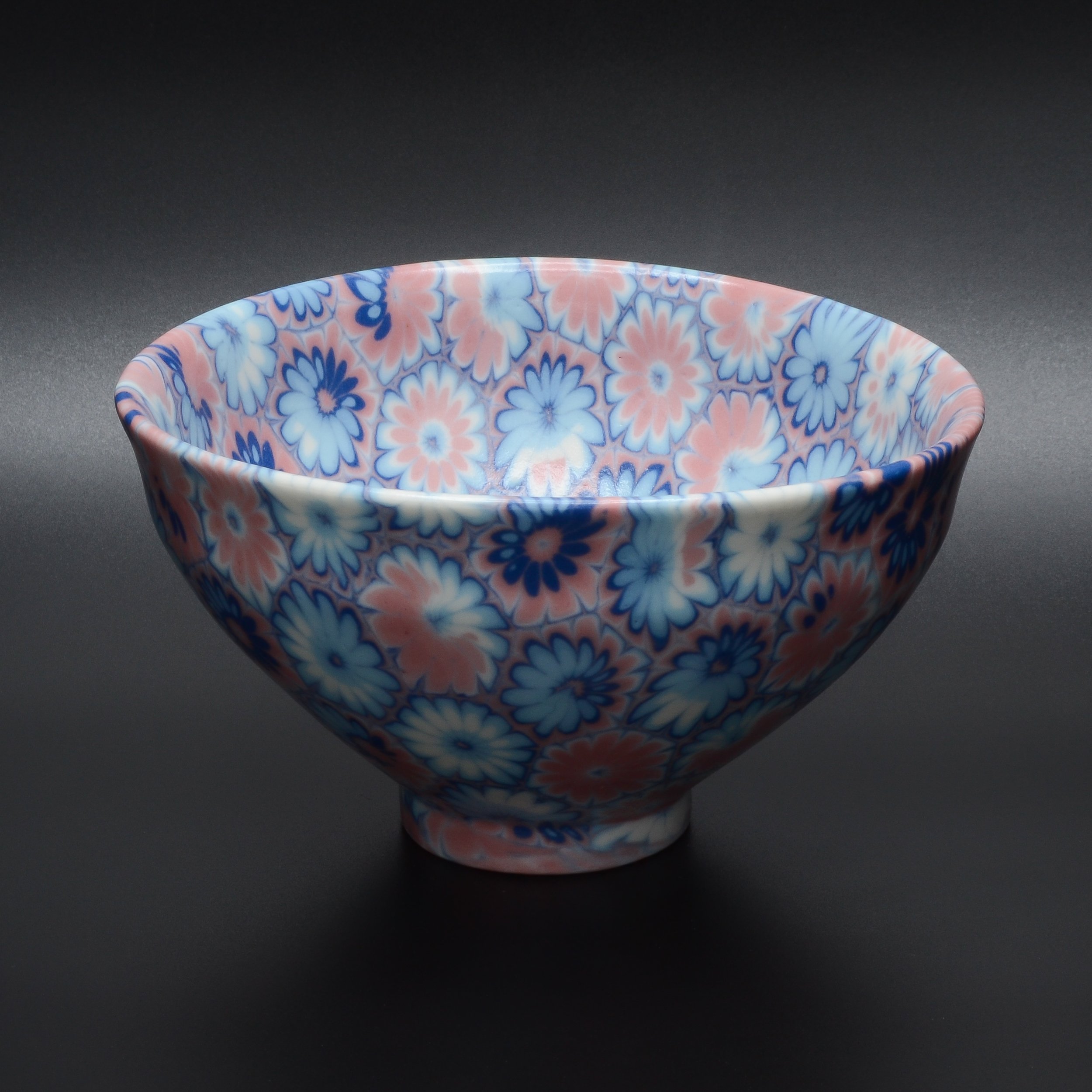 Assiette en céramique avec motif floral en couleurs pastel, vue de dessus, sur fond noir.