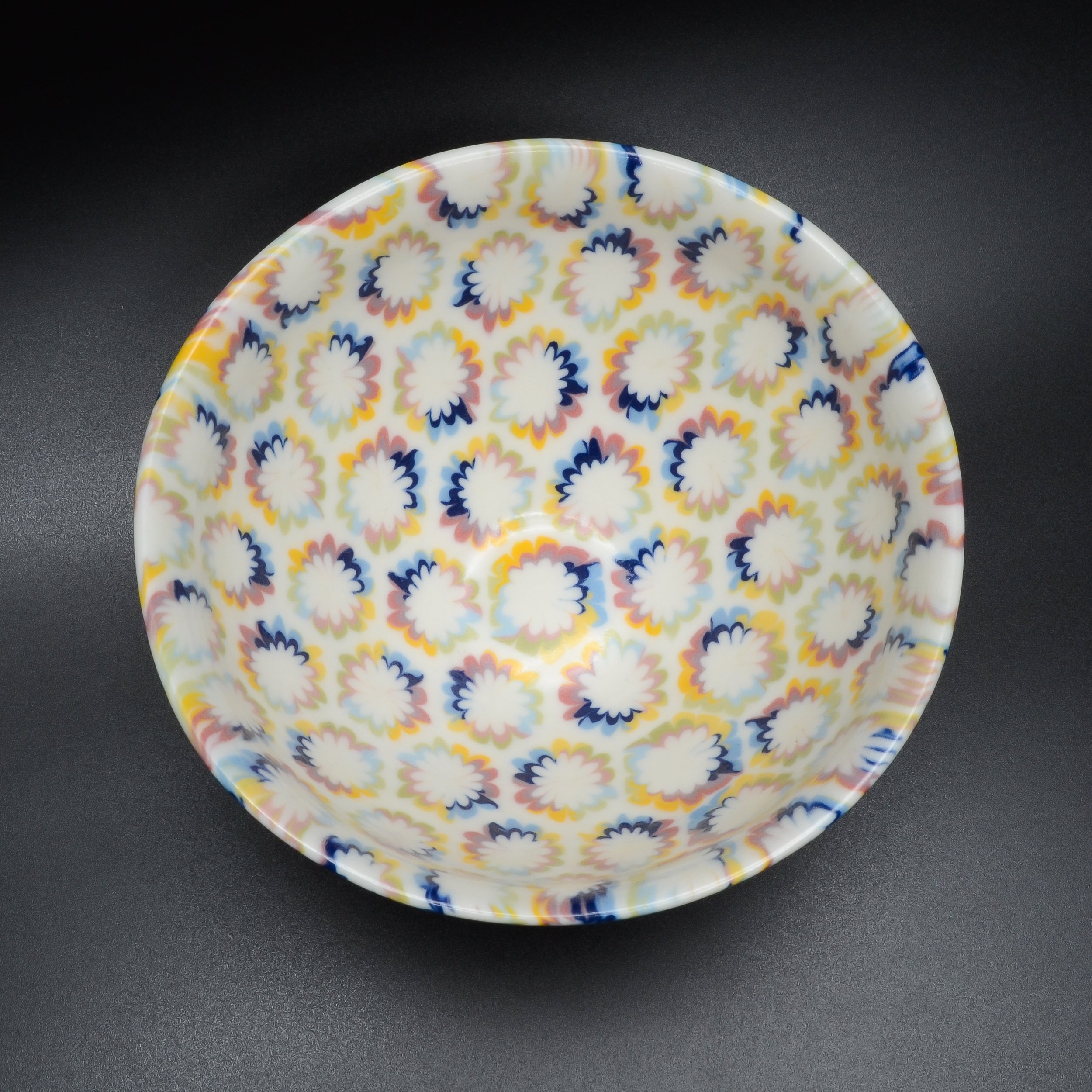 Assiette en céramique blanche avec un motif floral coloré en rose, bleu, jaune et vert, reposant sur une surface noire.
