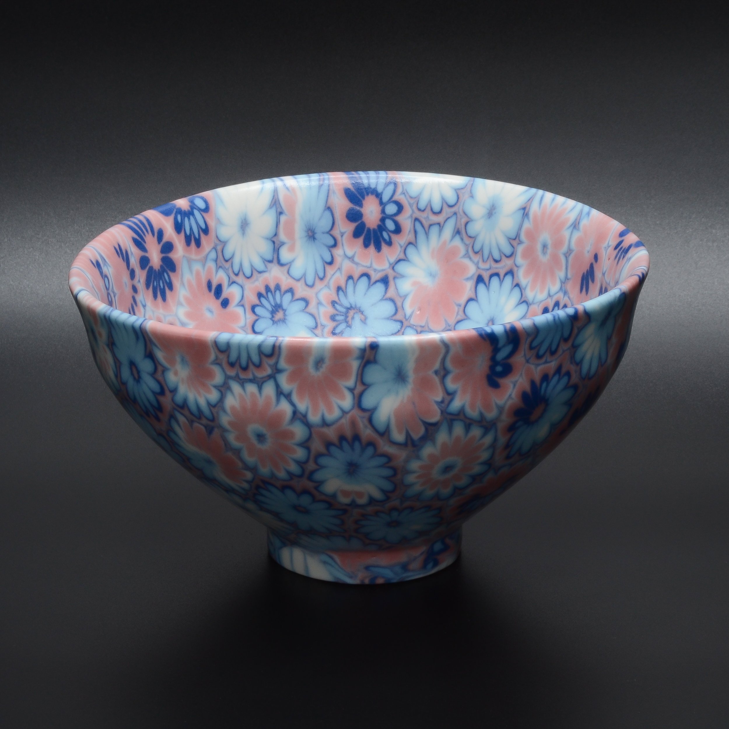 Un bol en céramique avec un motif floral bleu et rose sur un fond gris foncé.