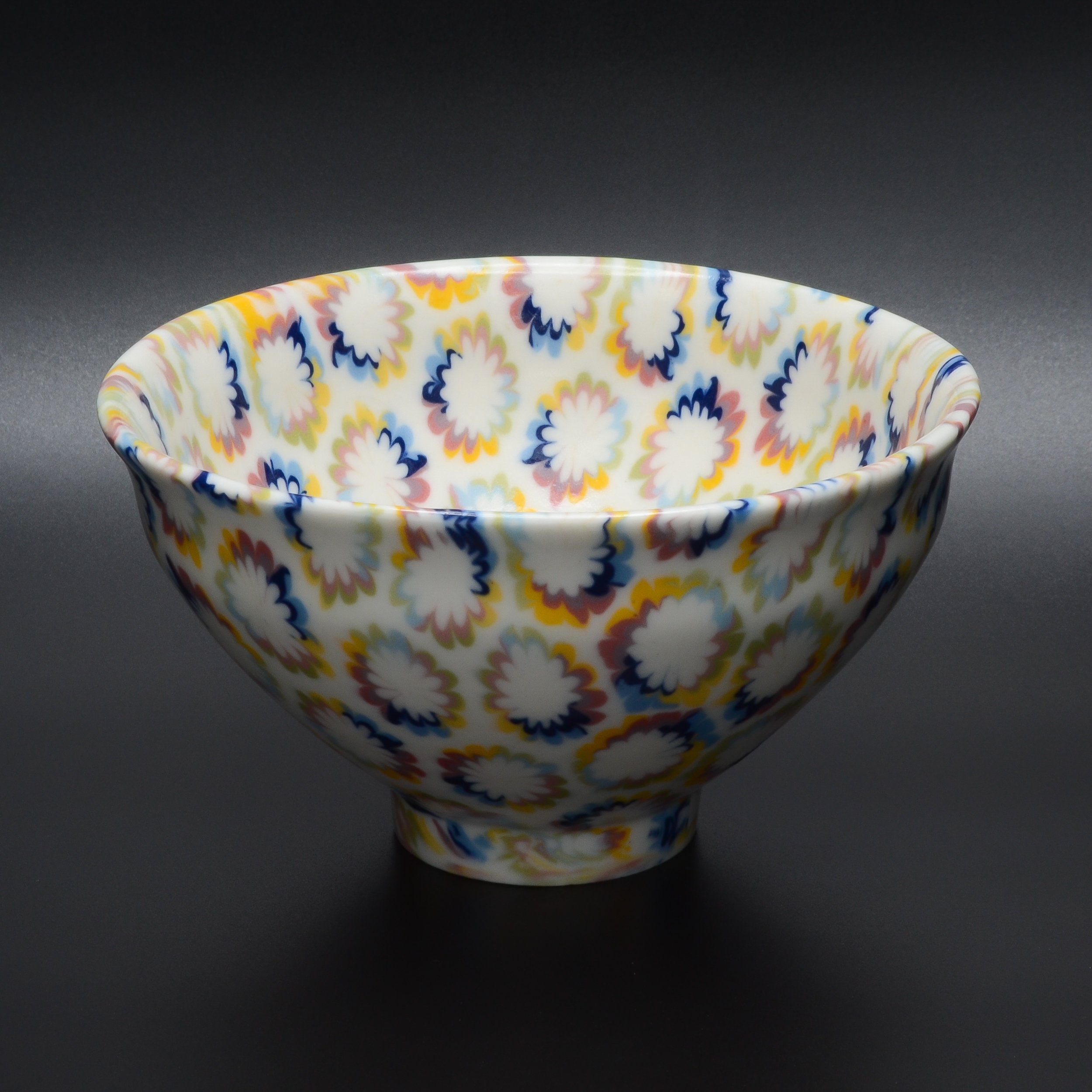 Un bol en porcelaine avec un motif coloré de fleurs en pastel sur fond blanc, posé sur une surface sombre.