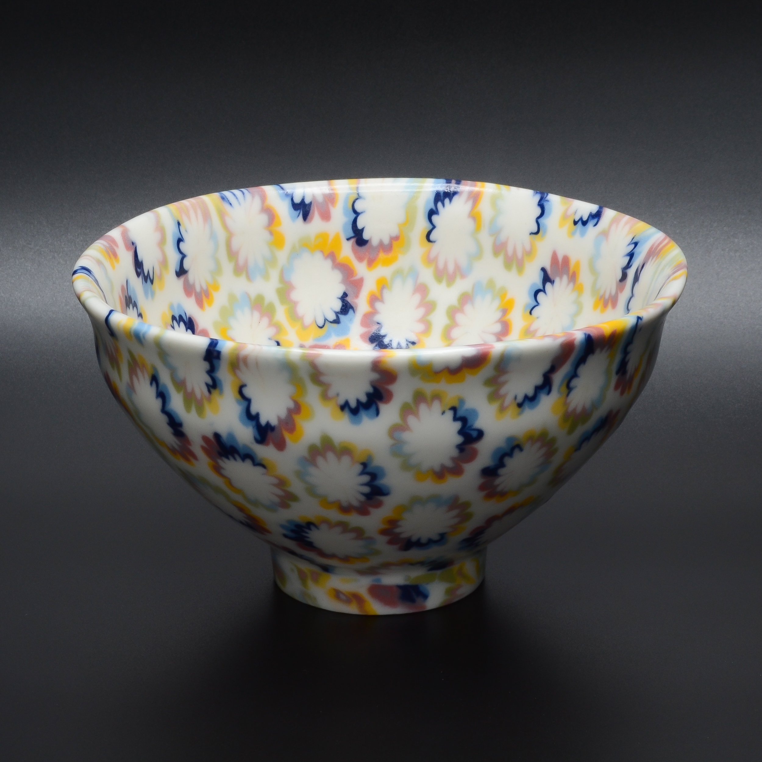 Bol en porcelaine avec un motif floral coloré, posé sur un fond gris foncé.