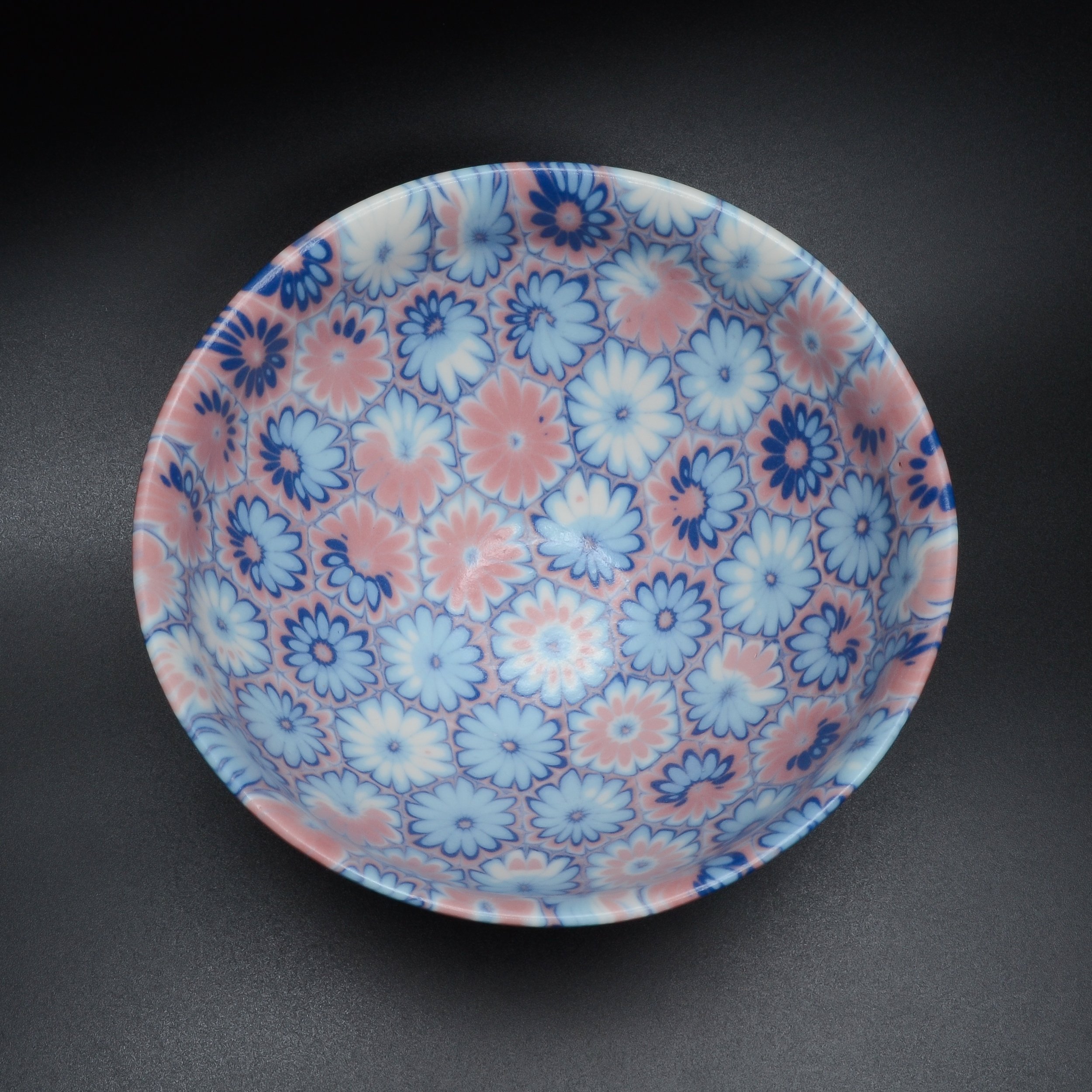 Assiette en céramique avec motif floral en bleu et rose, vue partielle sur fond noir.