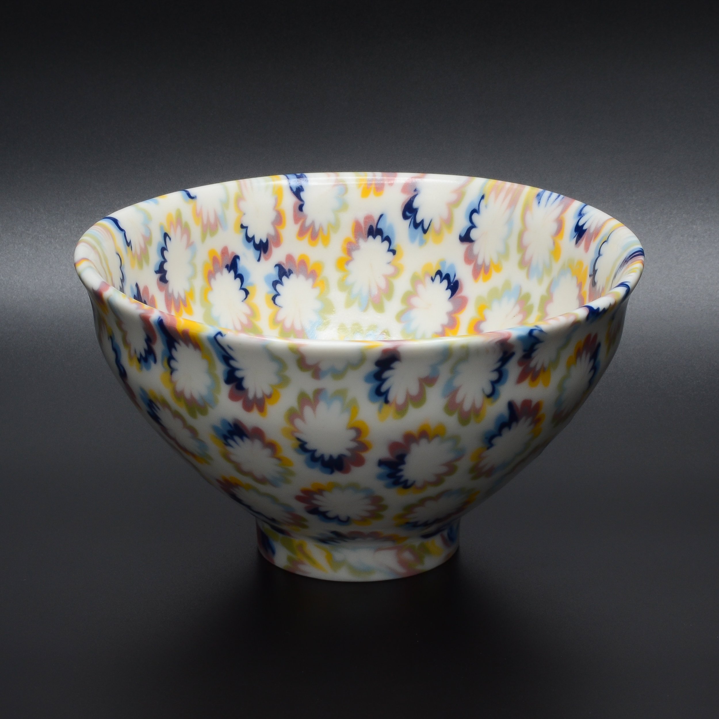 Un bol en céramique decoré avec un motif floral coloré, placé sur une surface noire.