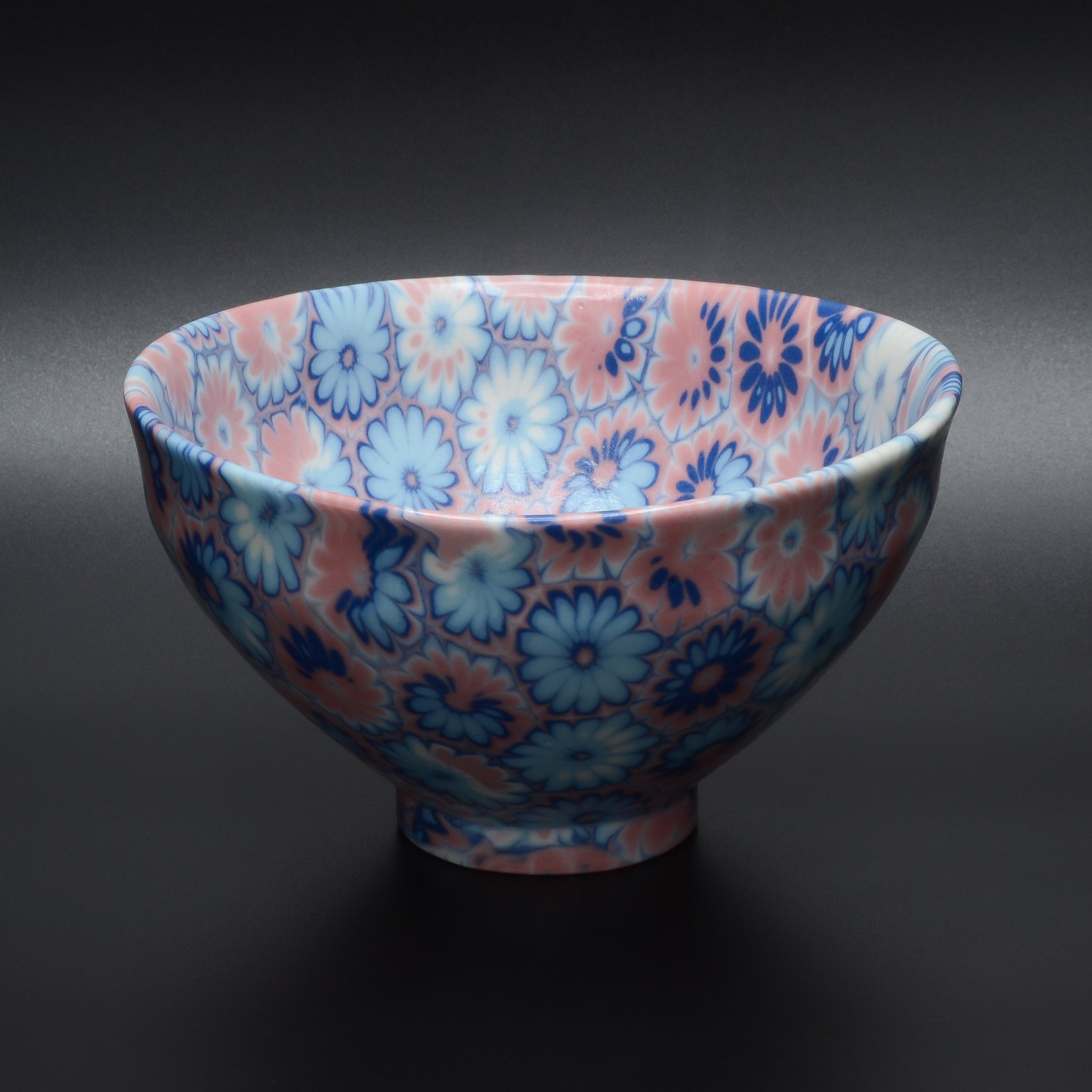 Un bol en porcelaine avec un motif floral rouge, blanc, et bleu clair, placé sur un fond noir.