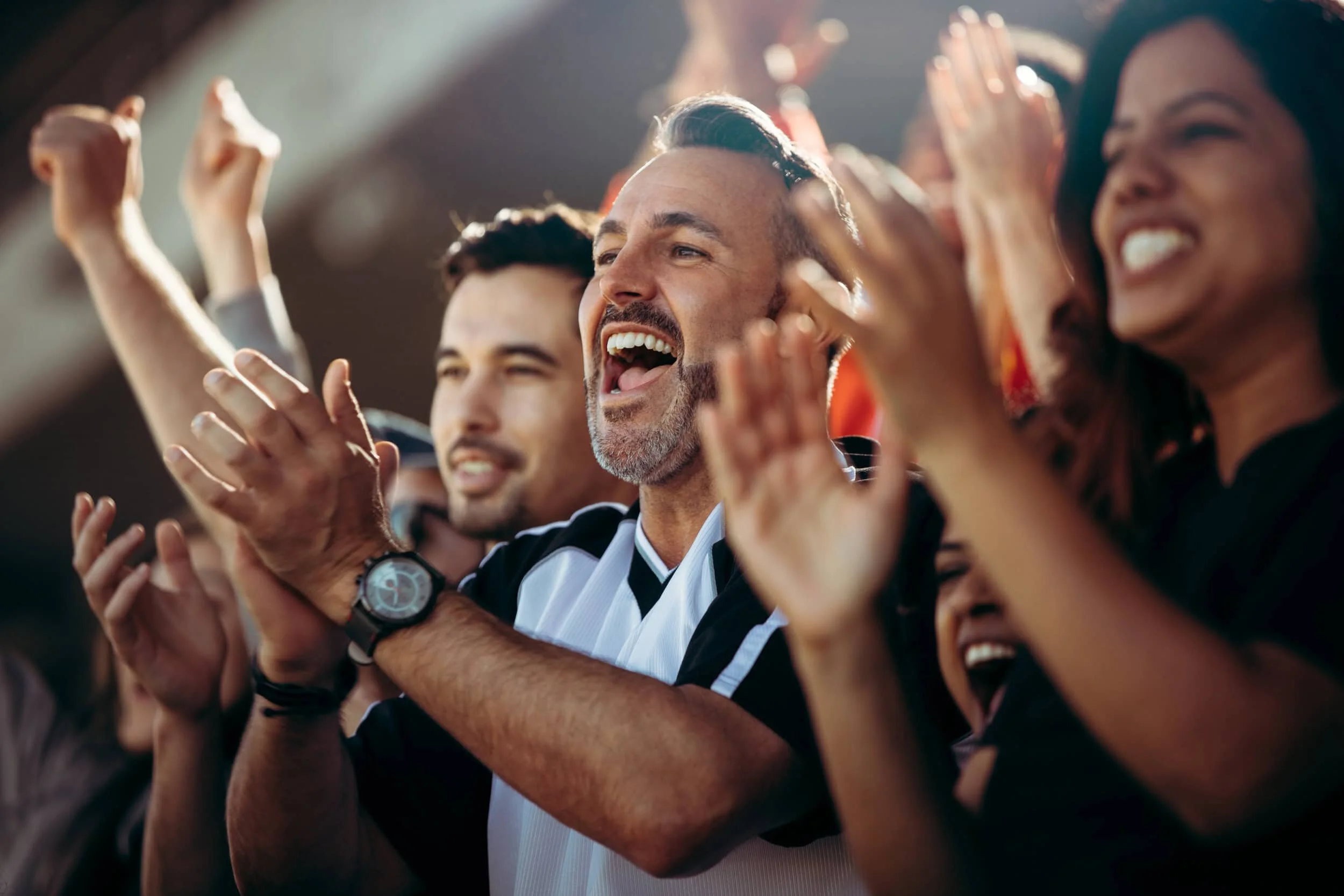 A group of people cheering and celebrating, some clapping and smiling, in a sports stadium.