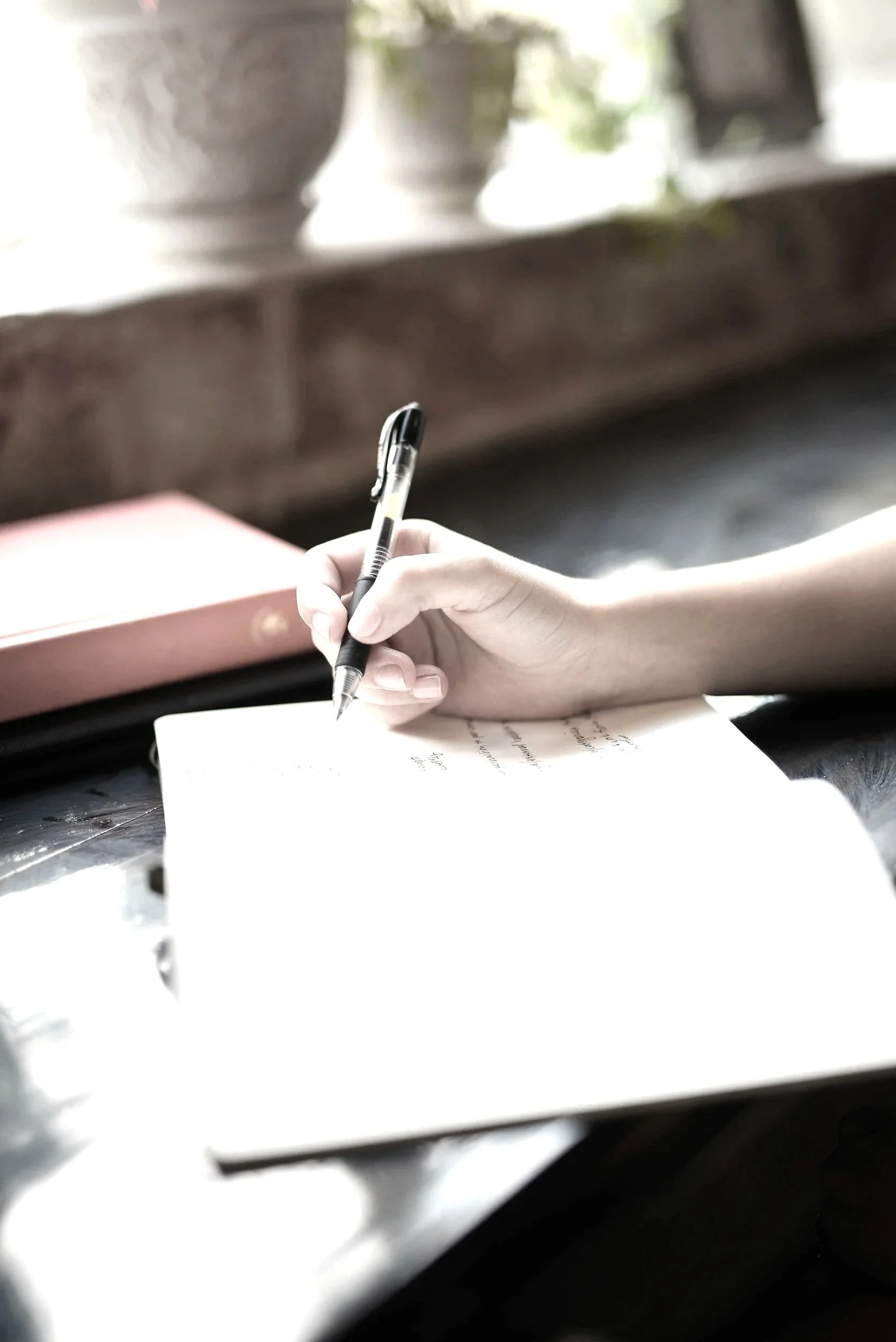 A person using a laptop at a wooden table with coffee cups, a backpack, and a portable charger.