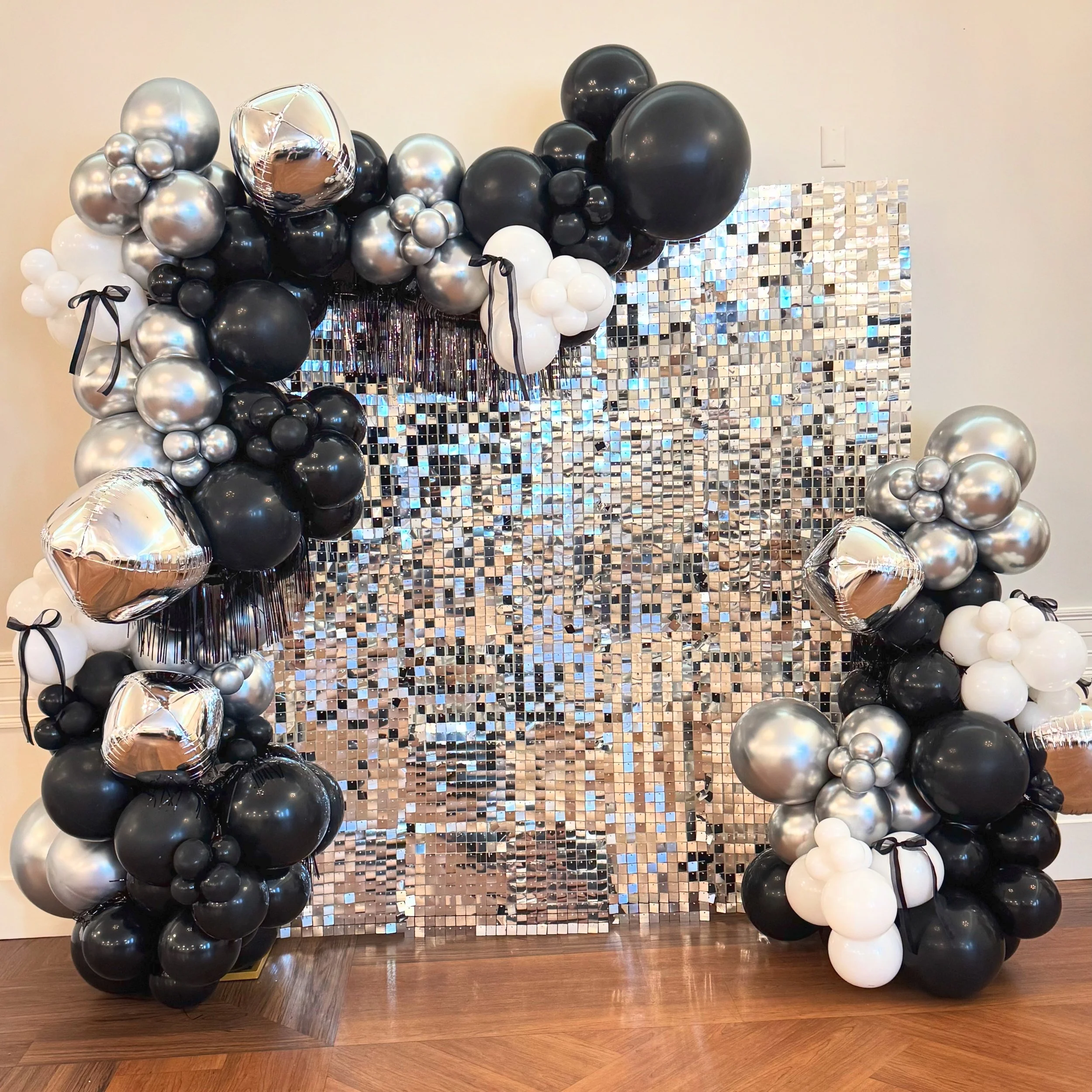 Black, white, and silver balloons arranged around a silver sequin backdrop for a celebration or event.