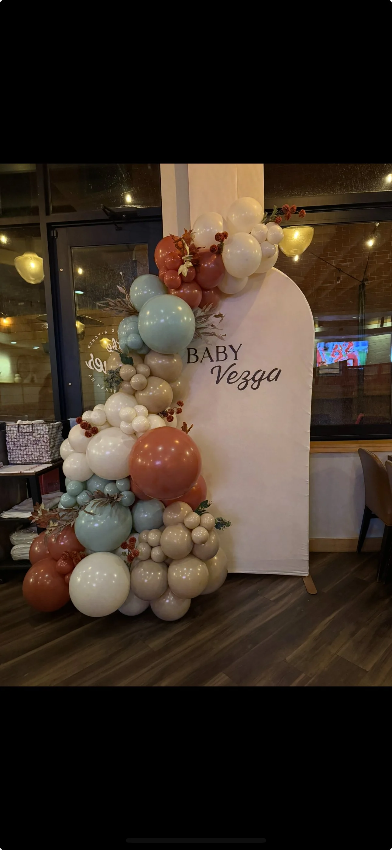 Balloon arrangement and a banner that reads 'Baby Vezza' in an indoor setting, likely for a baby shower or celebration.
