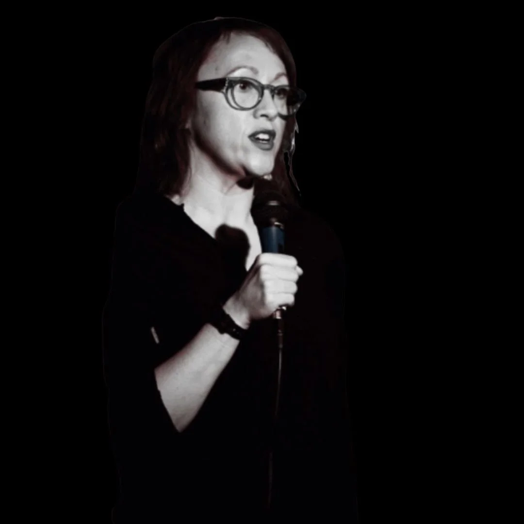 A black and white photo of a woman in glasses. She holds a mic and speaks.
