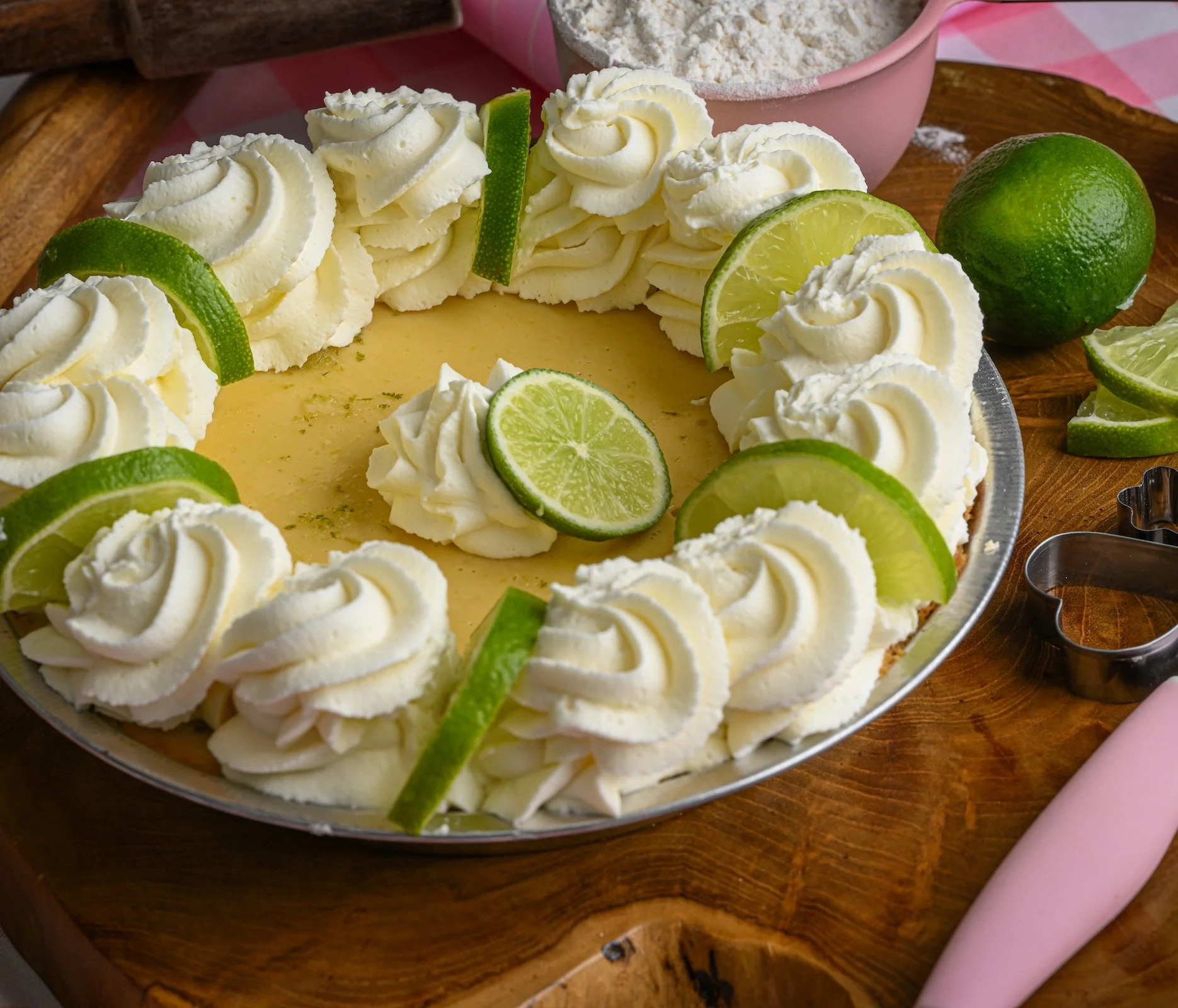 Lemon pie decorated with whipped cream and lime slices on top, placed on a wooden cutting board.
