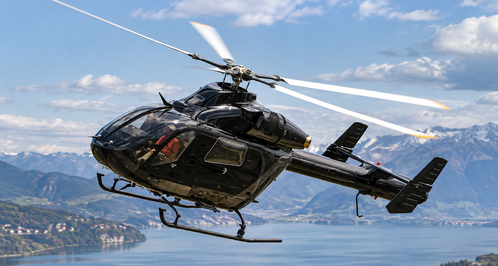 Black MD 900 Explorer twin-engine helicopter in flight above an Alpine lake, with mountains in the background.