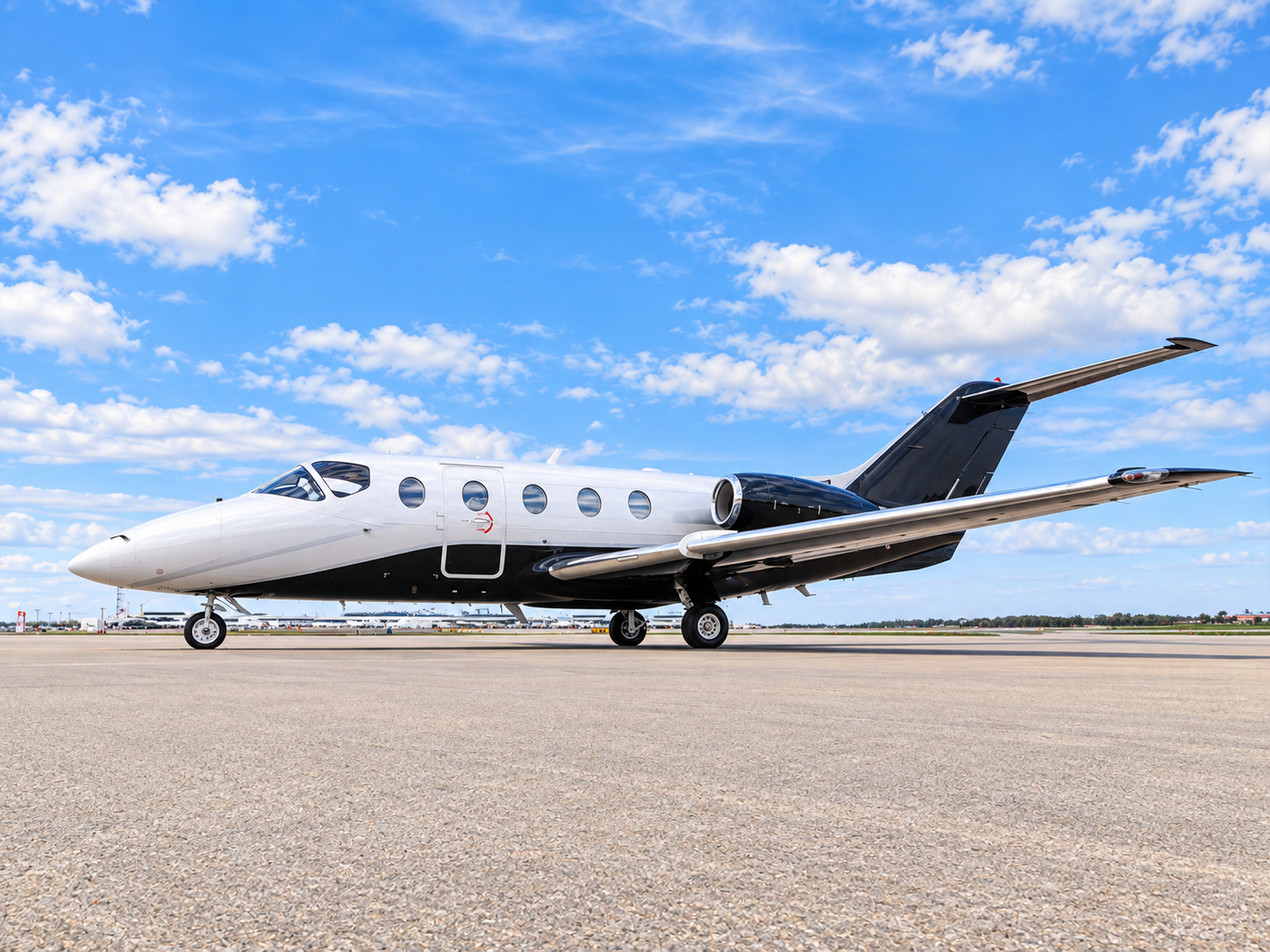 Nextant 400XTi private jet parked on an airport apron, shown in a bright exterior side view under a blue sky with scattered clouds.