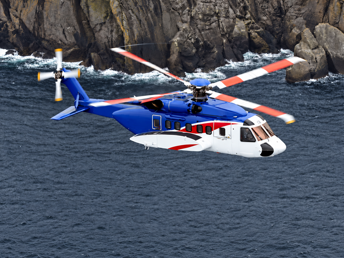 Sikorsky S-92 twin-engine VIP helicopter flying above the sea near a rocky coastline.