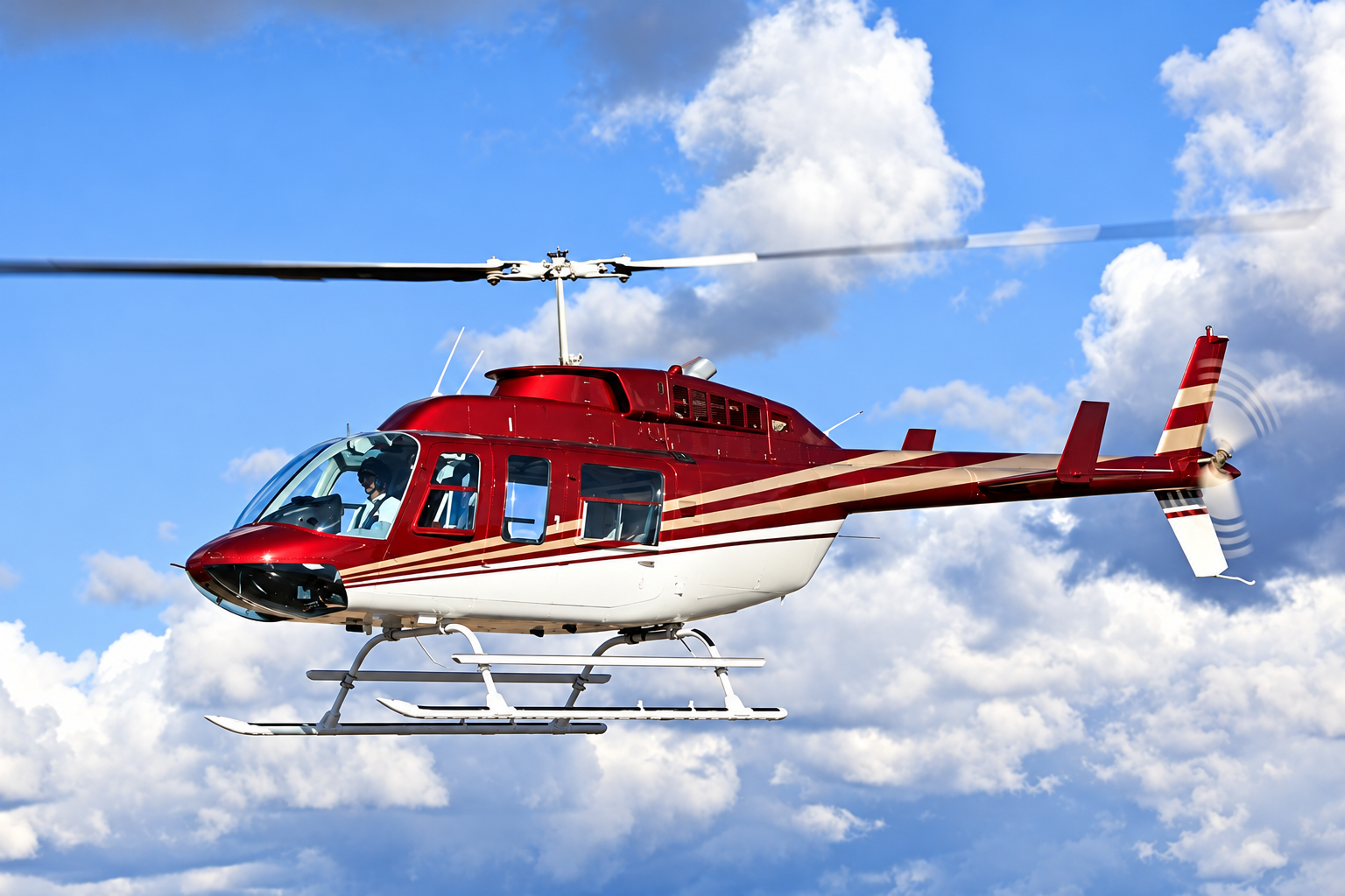 Bell 206 LongRanger single-engine helicopter in flight against a blue sky with clouds.