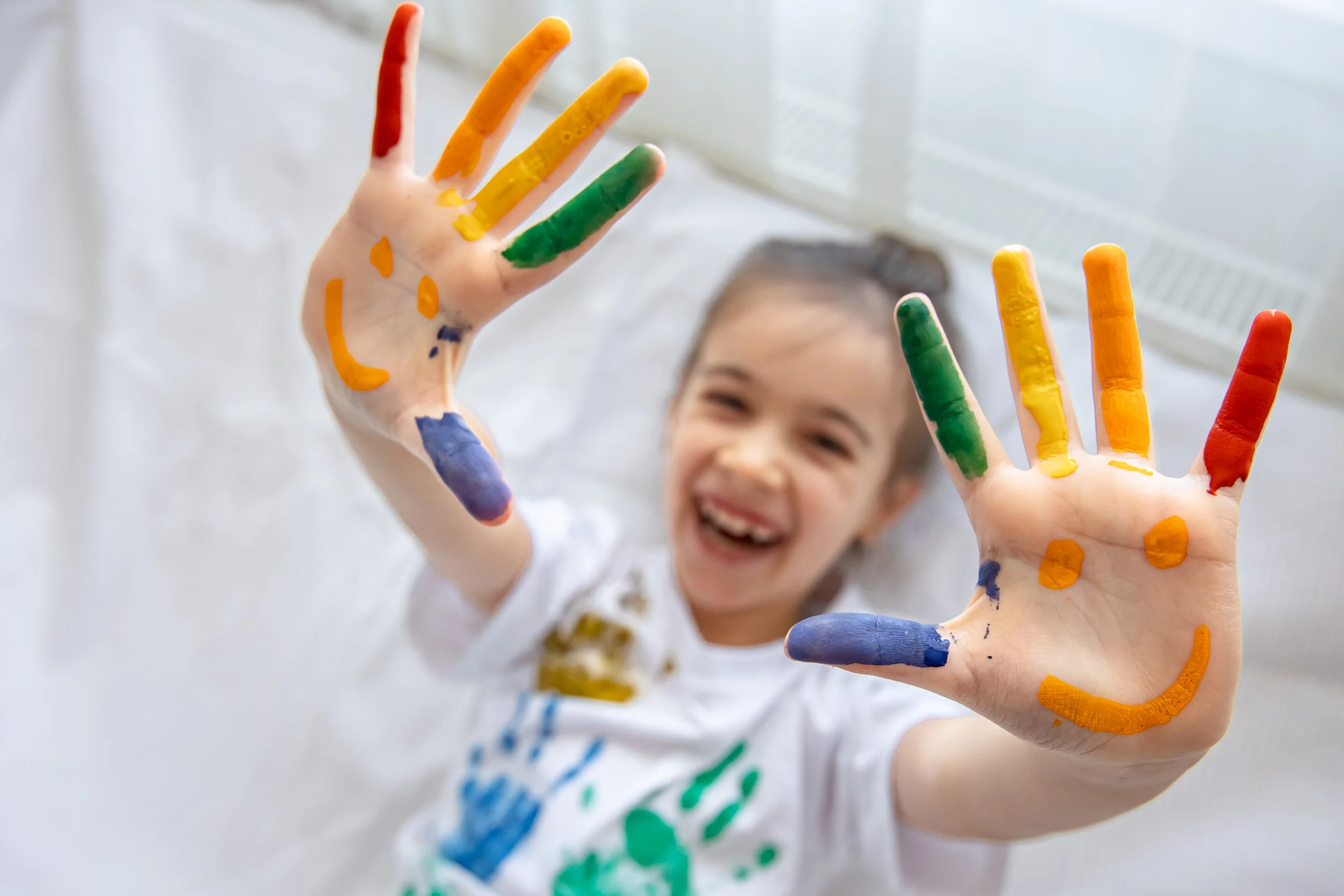 Happy young girl showing her colorful paint-covered hands, representing the joyful and playful approach to pediatric occupational therapy at Flourish Therapy Service in Athens, GA.