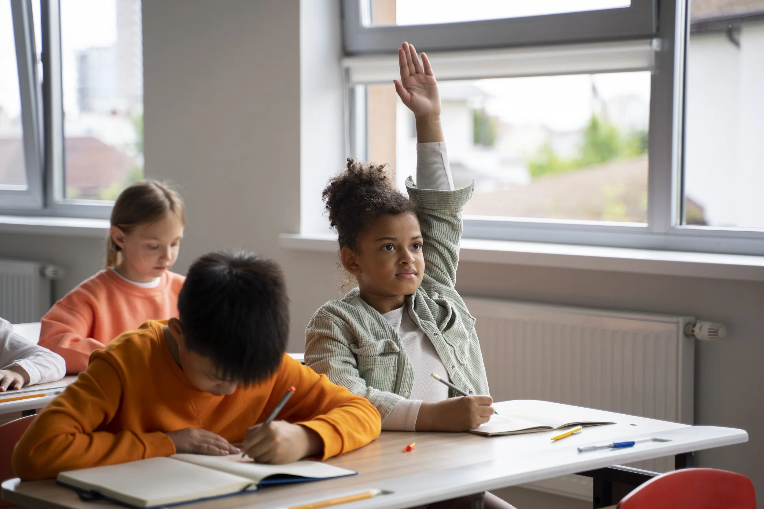 Children engaged in a classroom setting with one child confidently raising their hand, representing the growth in independence and self-confidence supported by pediatric occupational therapy services at Flourish Therapy Service in Athens, GA.