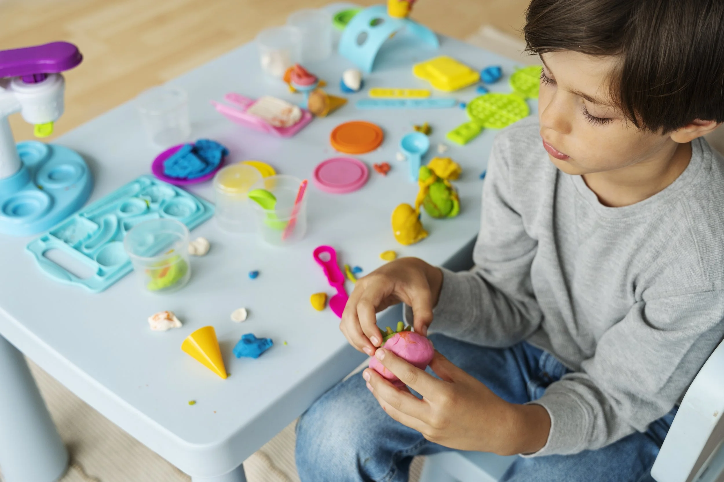 Child engaged in sensory play with colorful toys at a table, supporting fine motor and sensory processing development through pediatric occupational therapy at Flourish Therapy Service in Athens, GA.