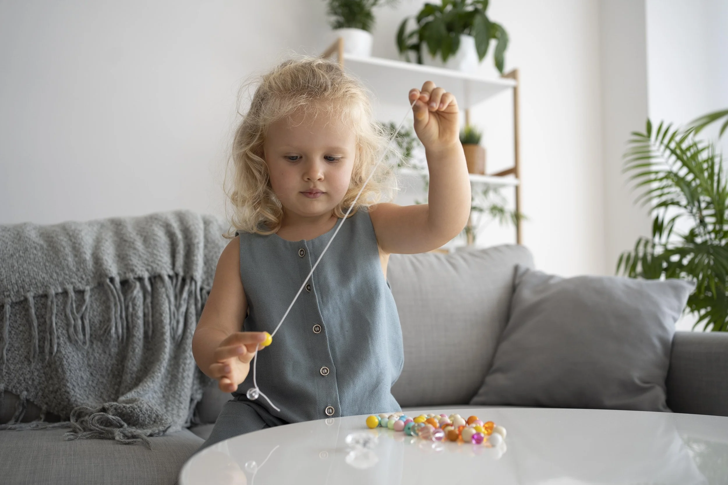 Young girl practicing fine motor skills by threading beads at home, representing the flexible and family-centered occupational therapy services provided by Flourish Therapy Service in Athens, GA.